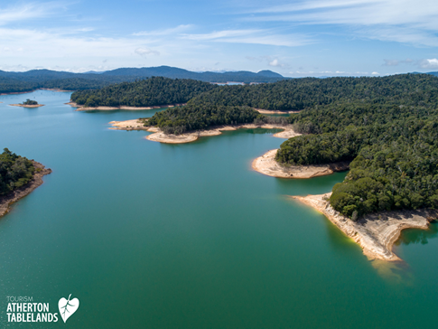 Aerial view of a turquoise lake surrounded by green forested hills under a blue sky.