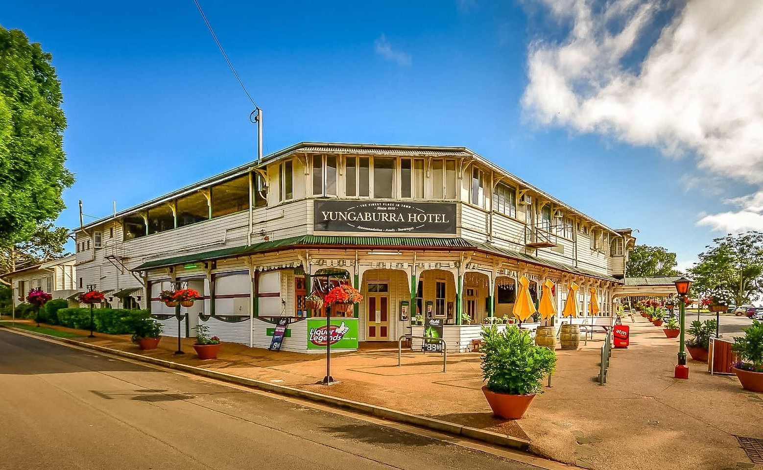 Historic two-story white hotel with green accents and a wraparound veranda on a sunny street.