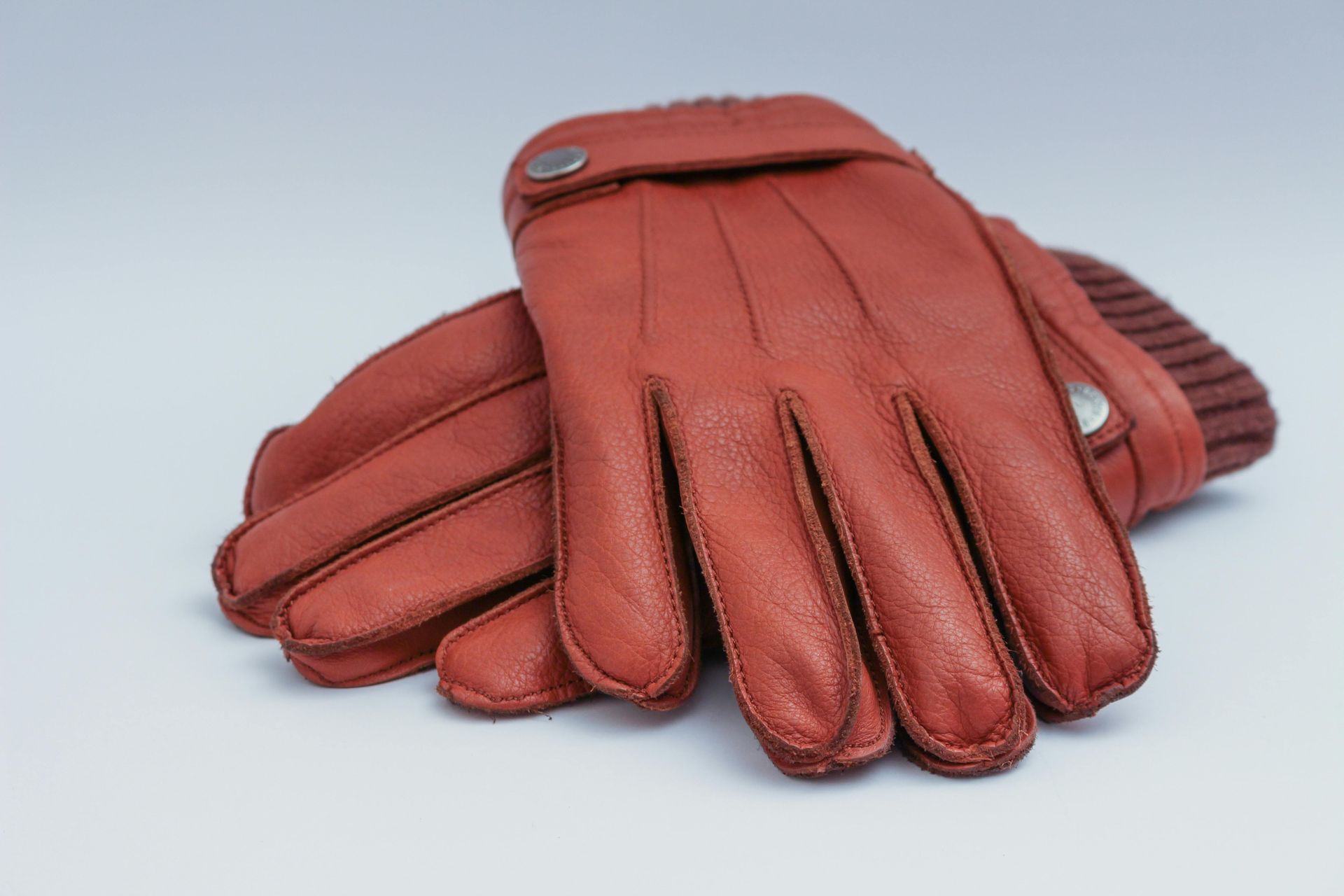 A pair of brown leather gloves on a white surface