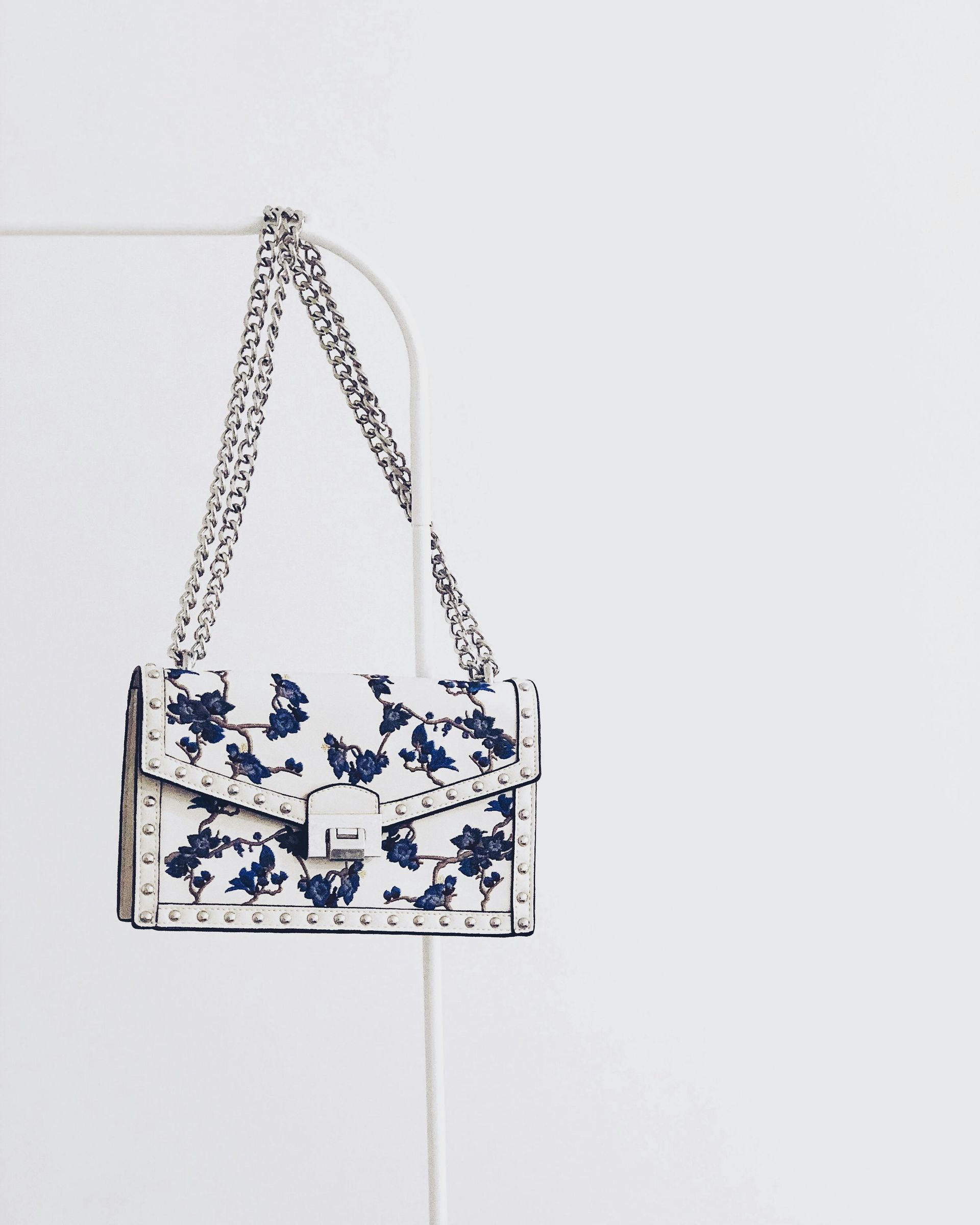 A white purse with blue flowers on it is hanging on a rack