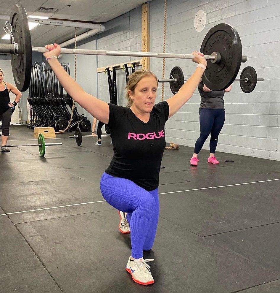 A woman is squatting down while holding a barbell over her head in a gym.