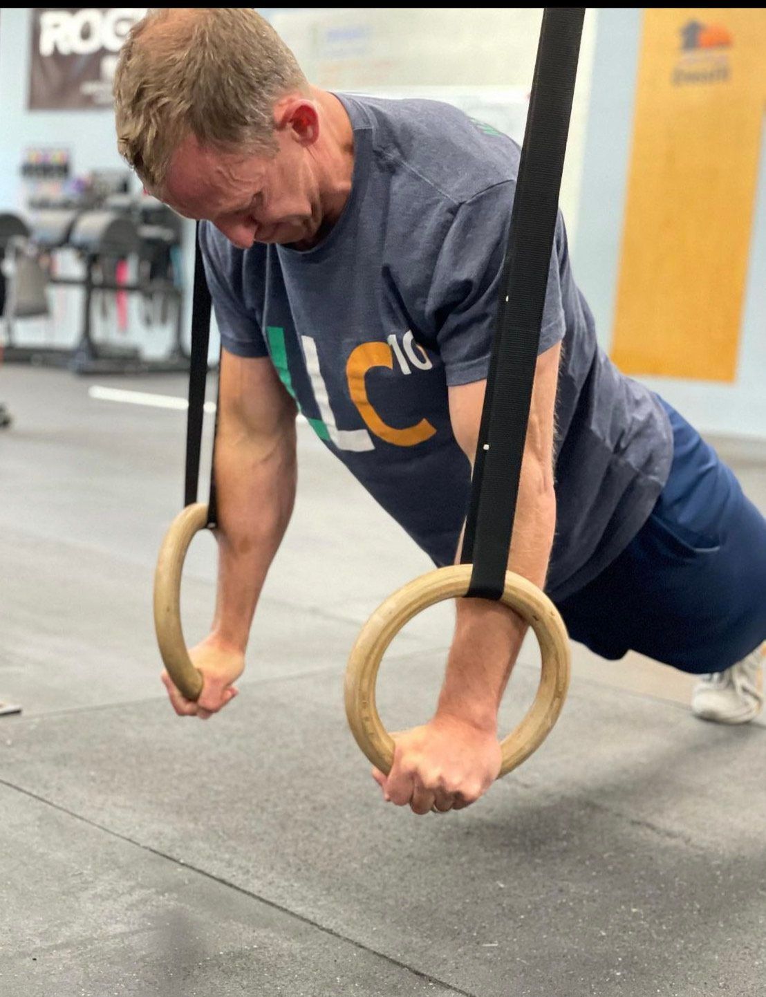 A man wearing a shirt that says lc is doing push ups on gymnastic rings