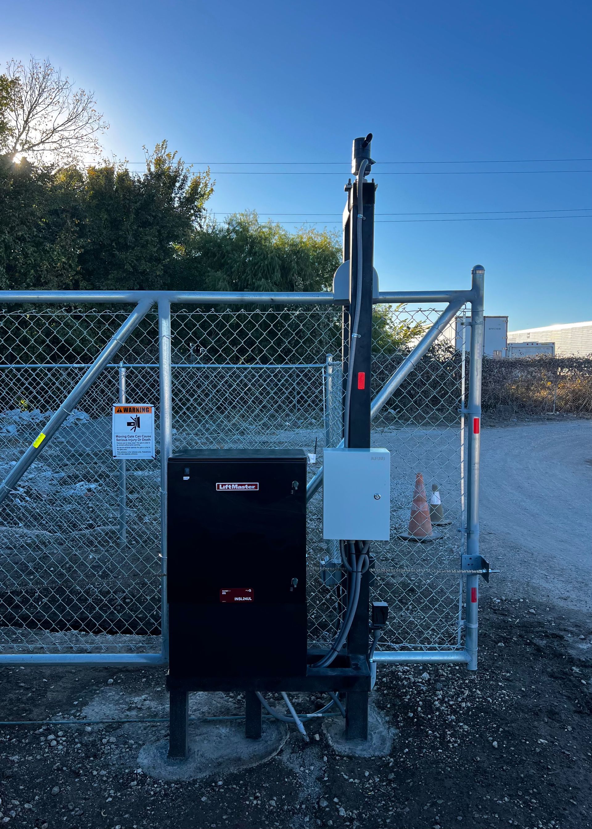 Automatic gate with control box, mounted on a concrete base, chain link fence in background.