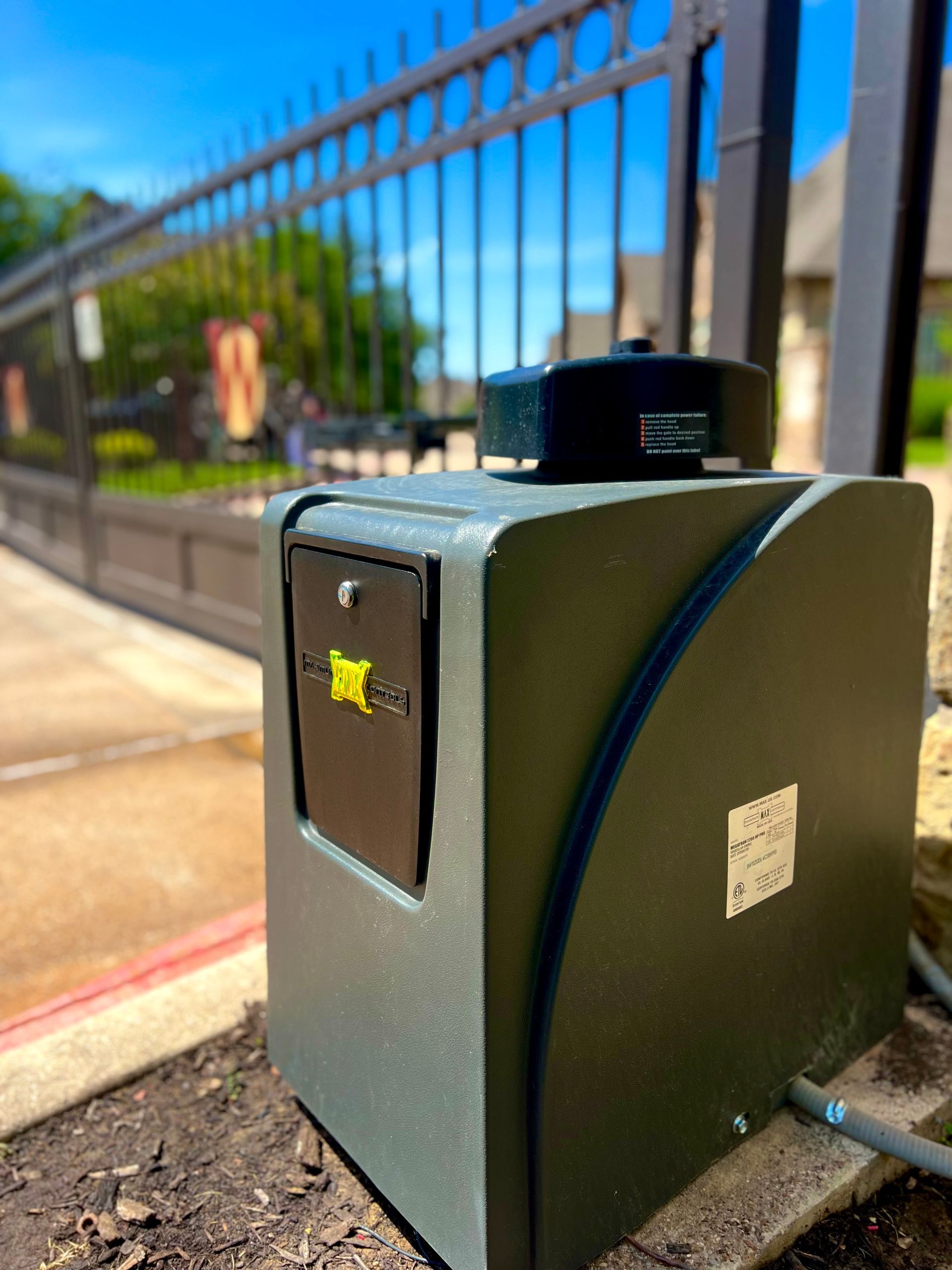 Dark green automatic gate opener box next to a black metal gate.