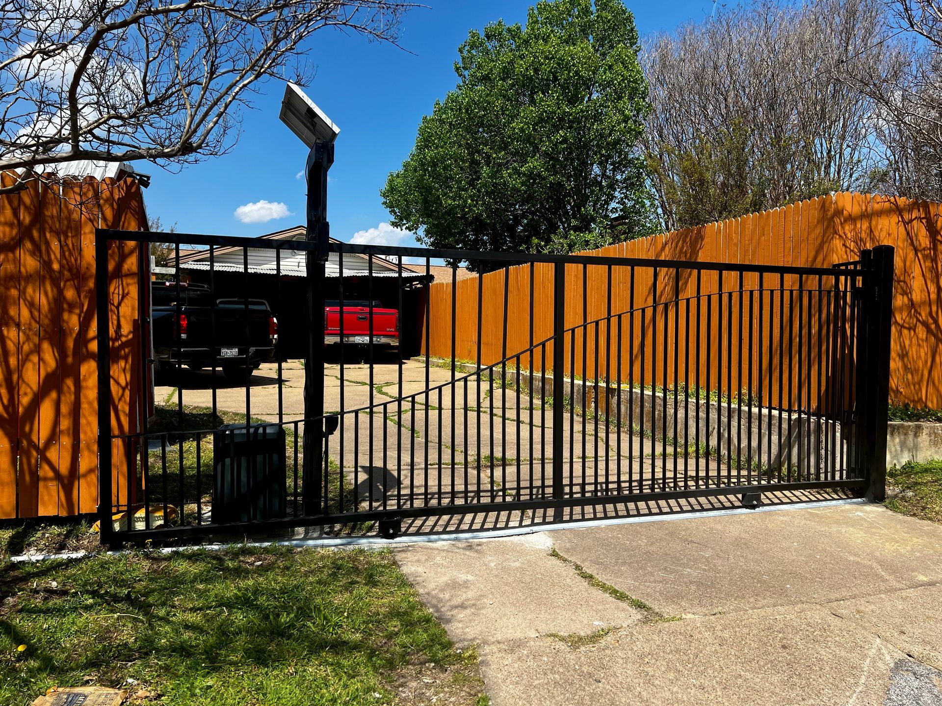 A black gate is open to a driveway with a red truck parked behind it.