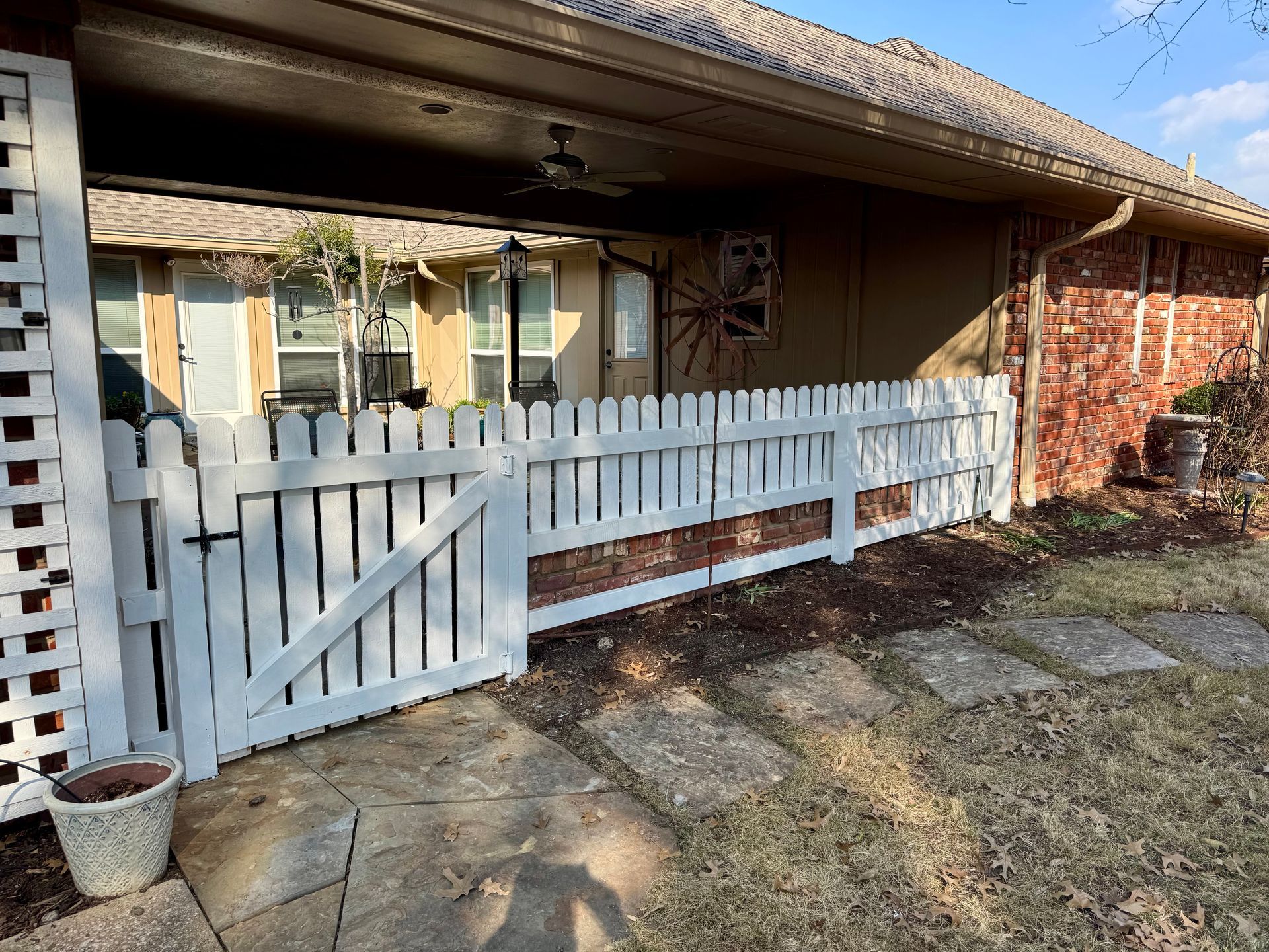 A white picket fence is in front of a brick house.
