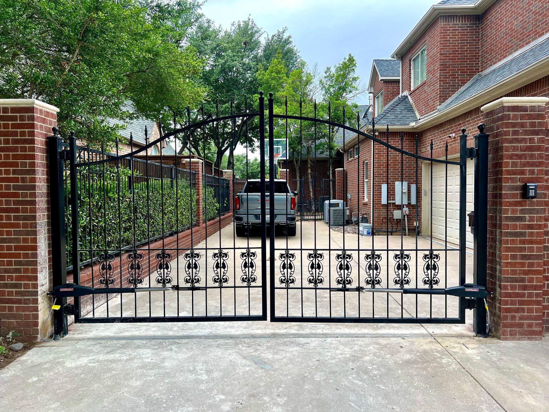 A black gate is open to a driveway in front of a brick house.