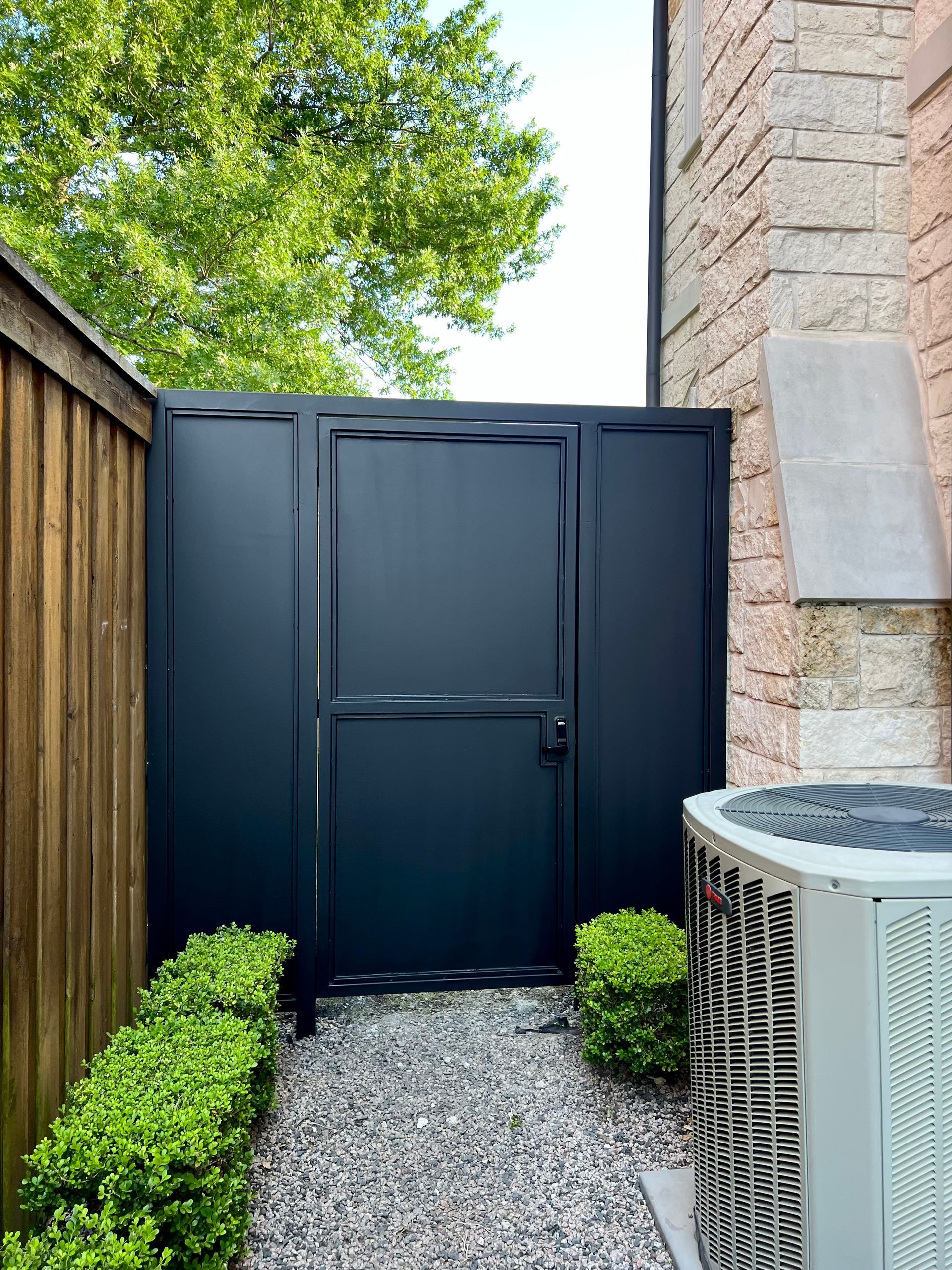 A black gate is between a brick building and a fence.