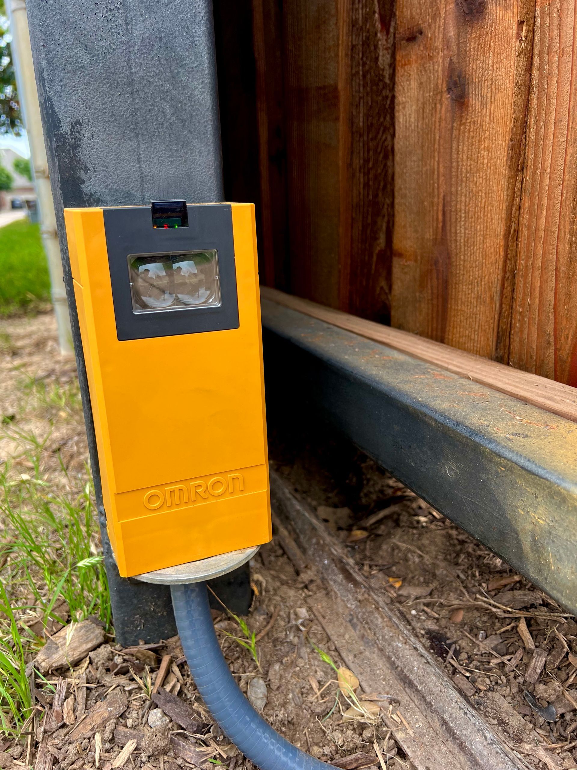 A yellow electrical outlet is plugged into a wooden fence.