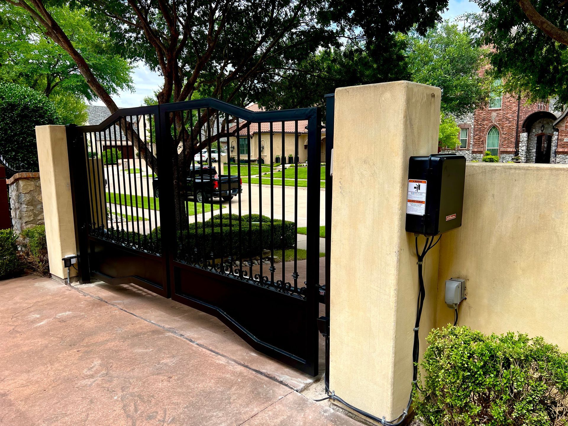 A black gate is open to a driveway in front of a house.