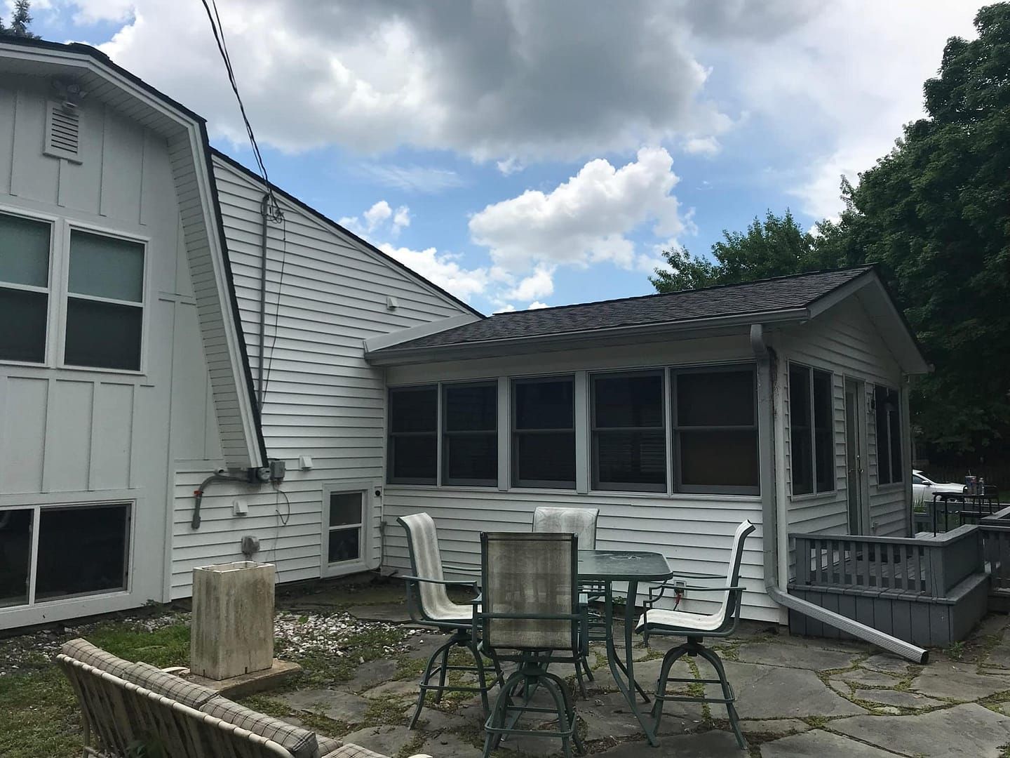 White house with attached screened-in patio, outdoor seating, and cloudy sky.