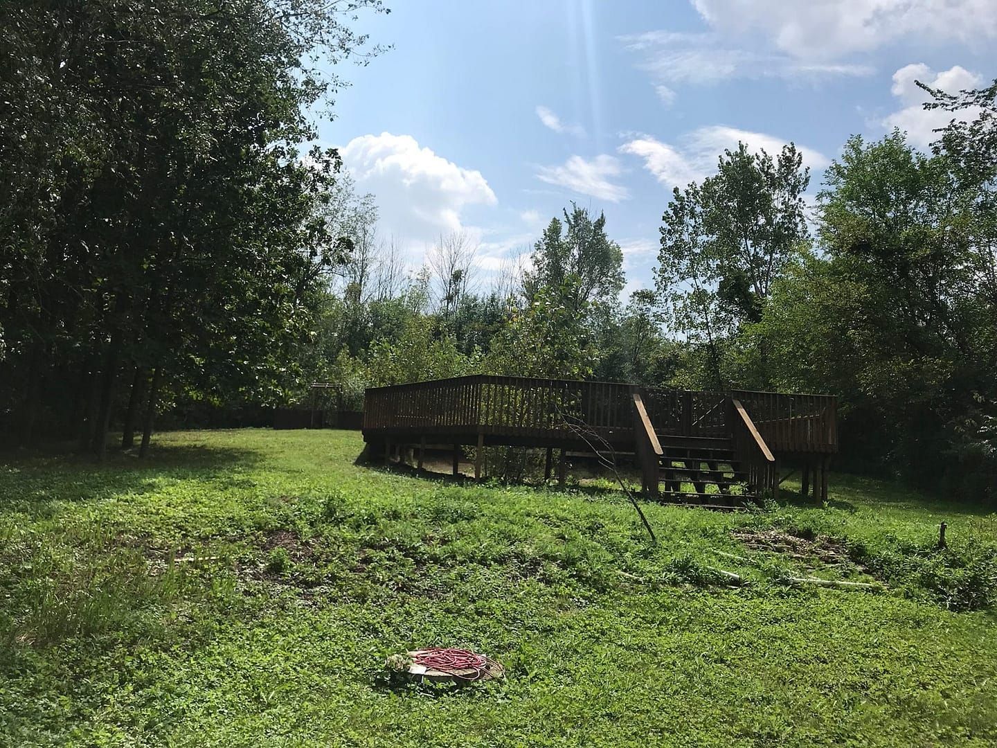 Wooden platform in a grassy field, surrounded by trees under a partly cloudy sky.