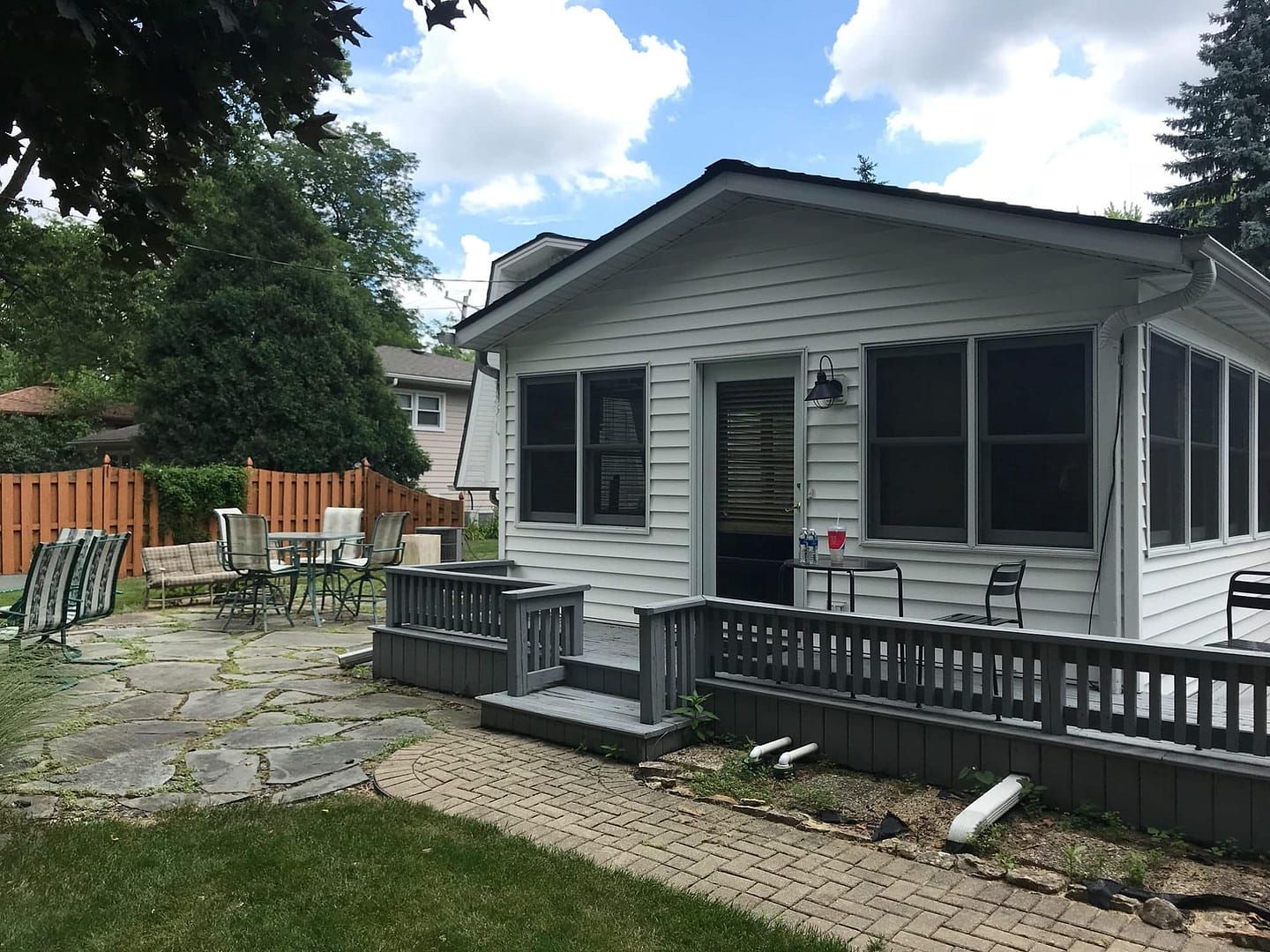 Backyard with patio, white house with dark trim, and gray deck with railing.