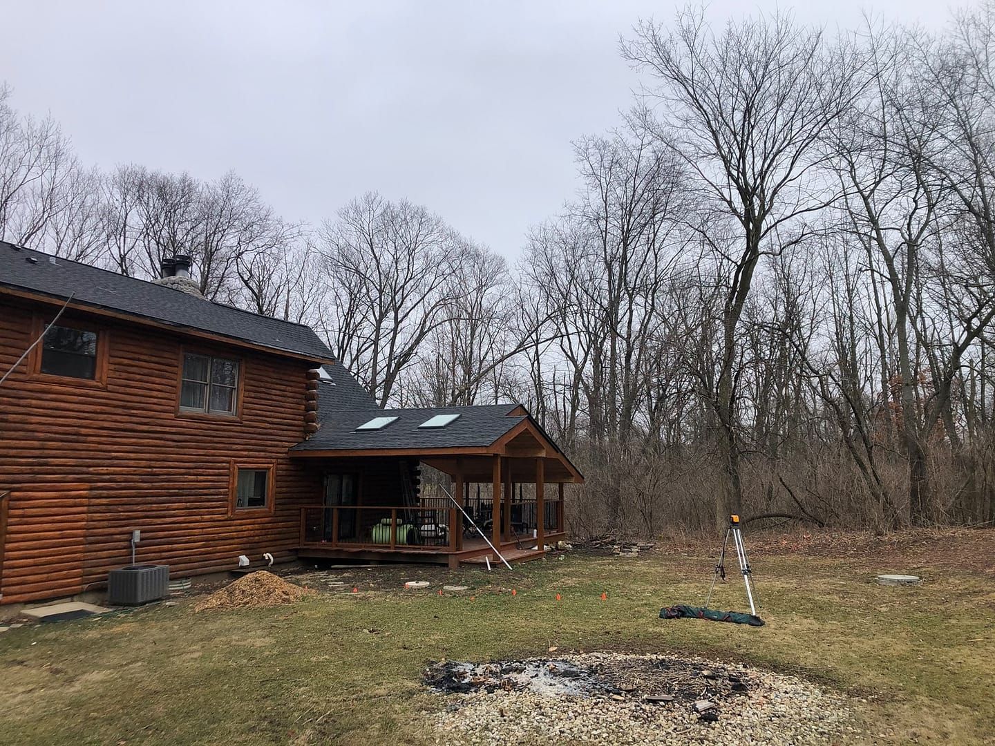 Wooden house with porch, trees, and a weed wacker in the backyard on a cloudy day.