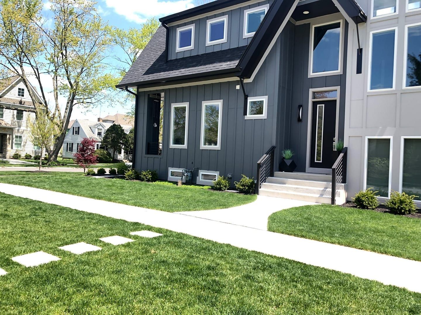 Modern gray house with large windows and walkway on a green lawn.