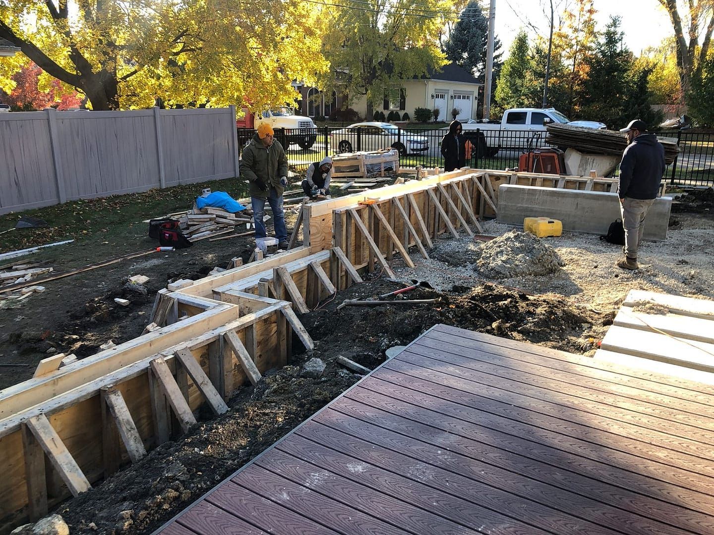 Construction workers building a retaining wall in a backyard. Wooden forms are in place, and concrete is visible.