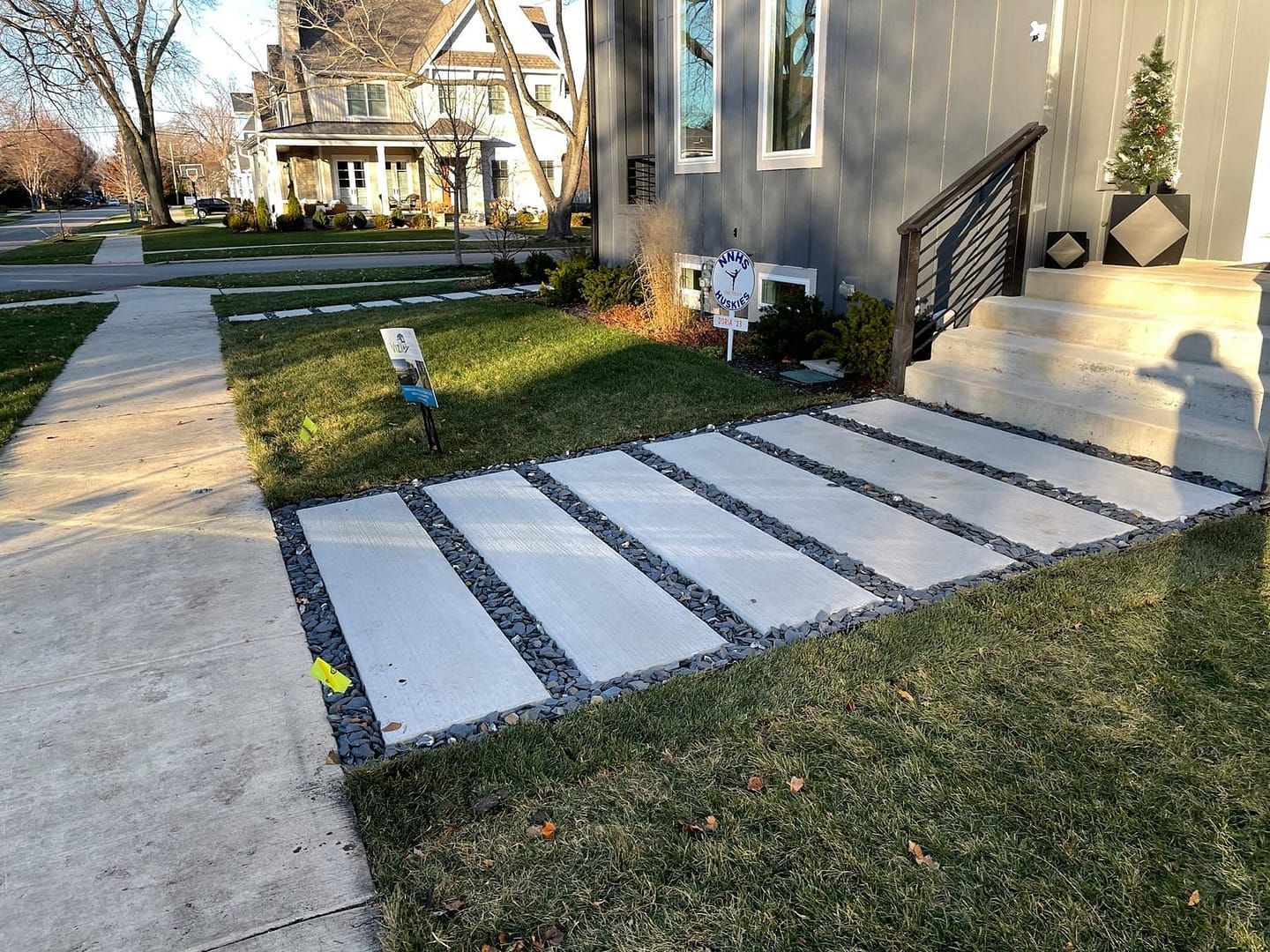 Concrete walkway with stone borders and green grass leading to a house entrance.