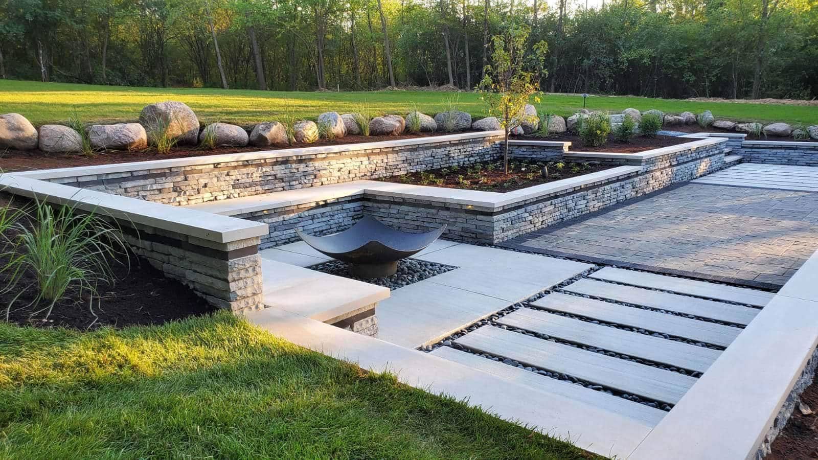 Stone patio with raised garden beds and a water feature in a grassy yard.