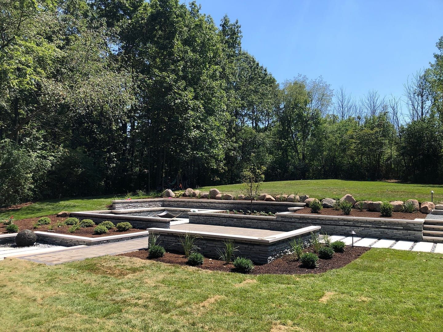 Stone tiered garden beds with landscaping and a grassy lawn.