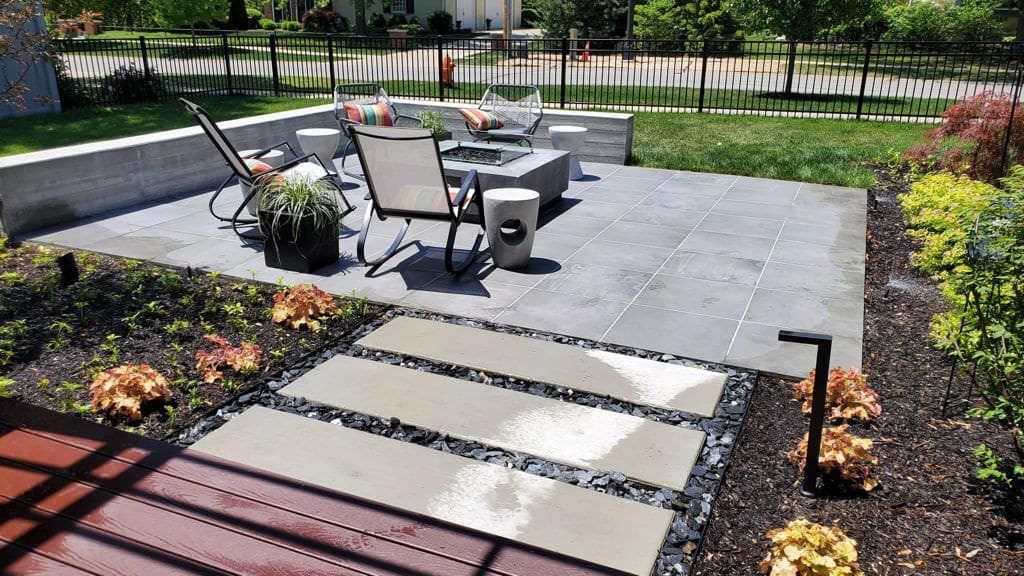 Patio with fire pit, seating, and stepping stones leading through a garden.