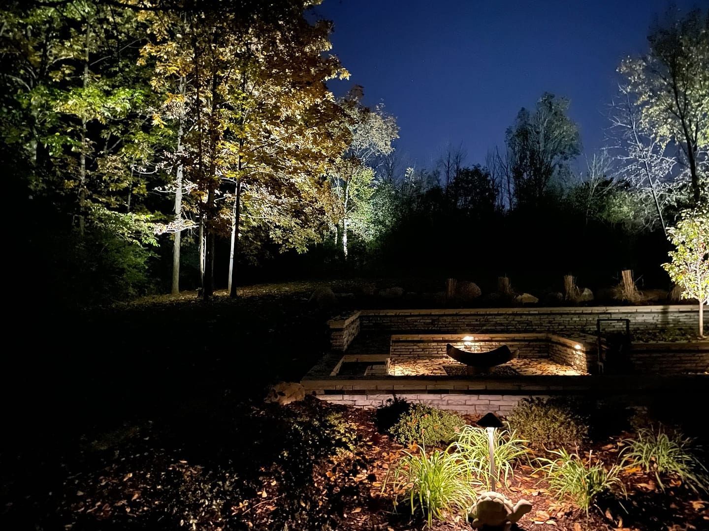 Night scene with spotlights illuminating trees and a tiered structure in a garden.