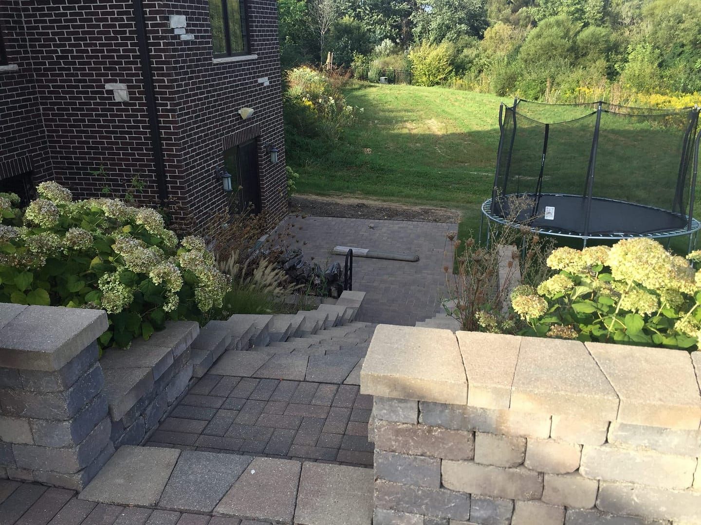 Stone steps lead down to a backyard with a trampoline and brick building. Hydrangeas line the steps.