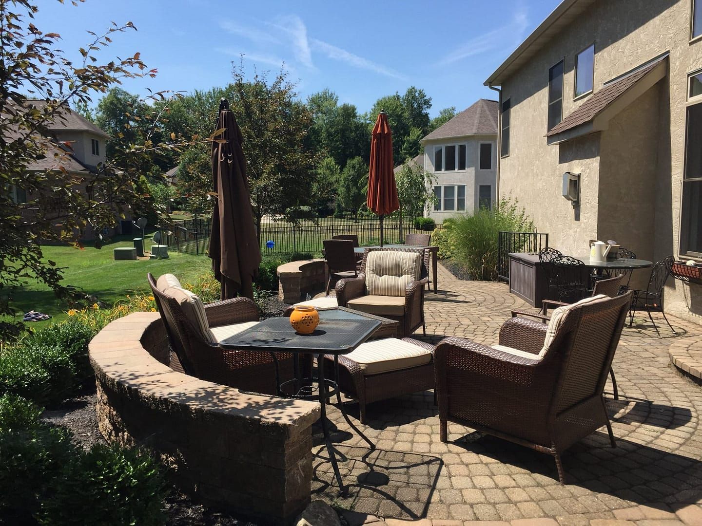 Patio with wicker furniture, umbrellas, and a table in a residential backyard on a sunny day.