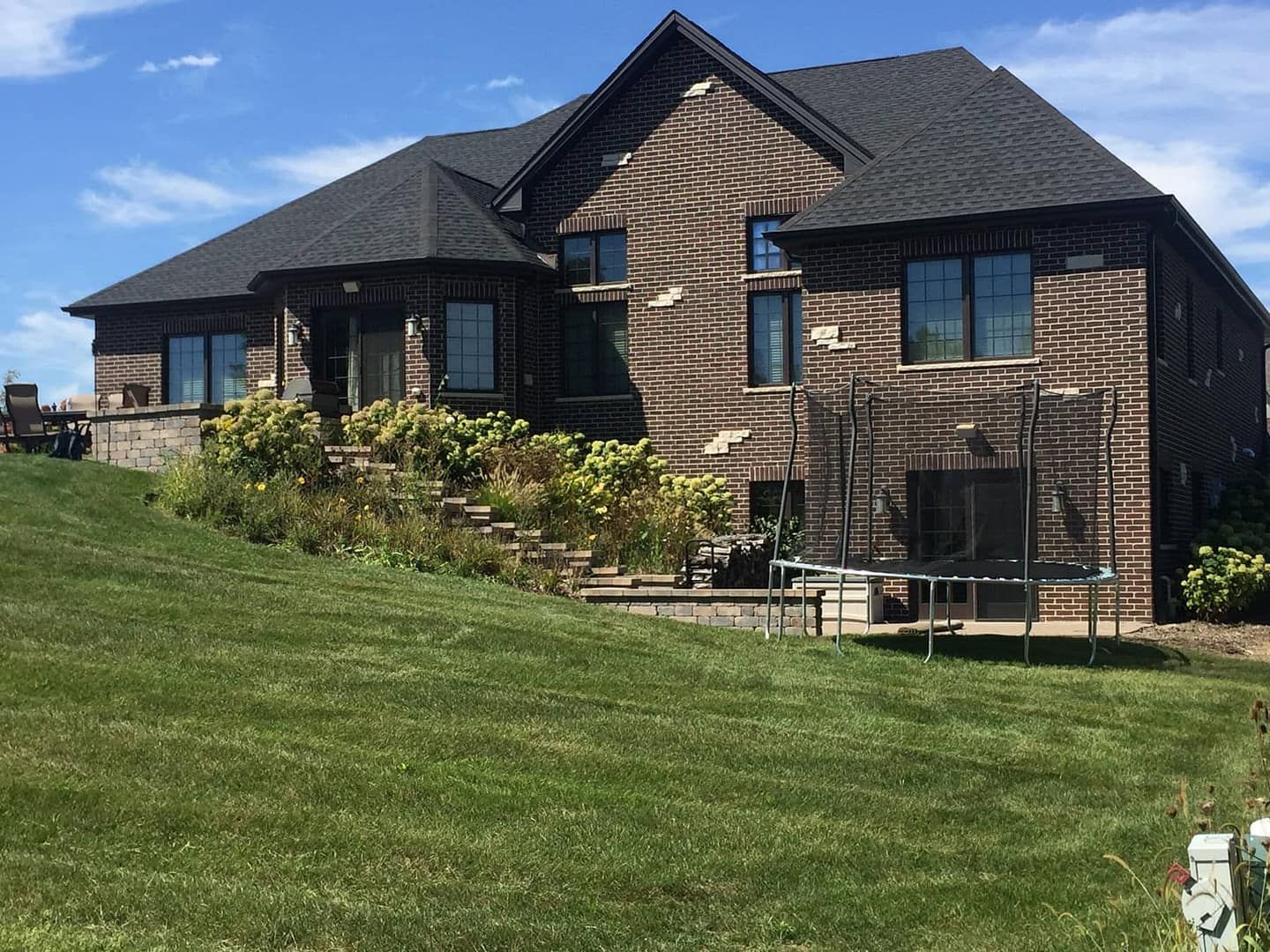 Brick house with dark roof, green lawn, and a trampoline on a sunny day.