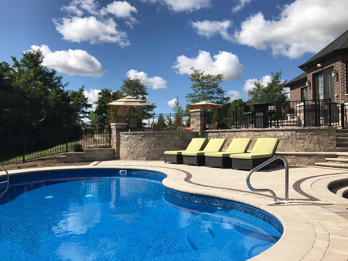 A backyard with a blue pool, lounge chairs, and a stone patio on a sunny day.