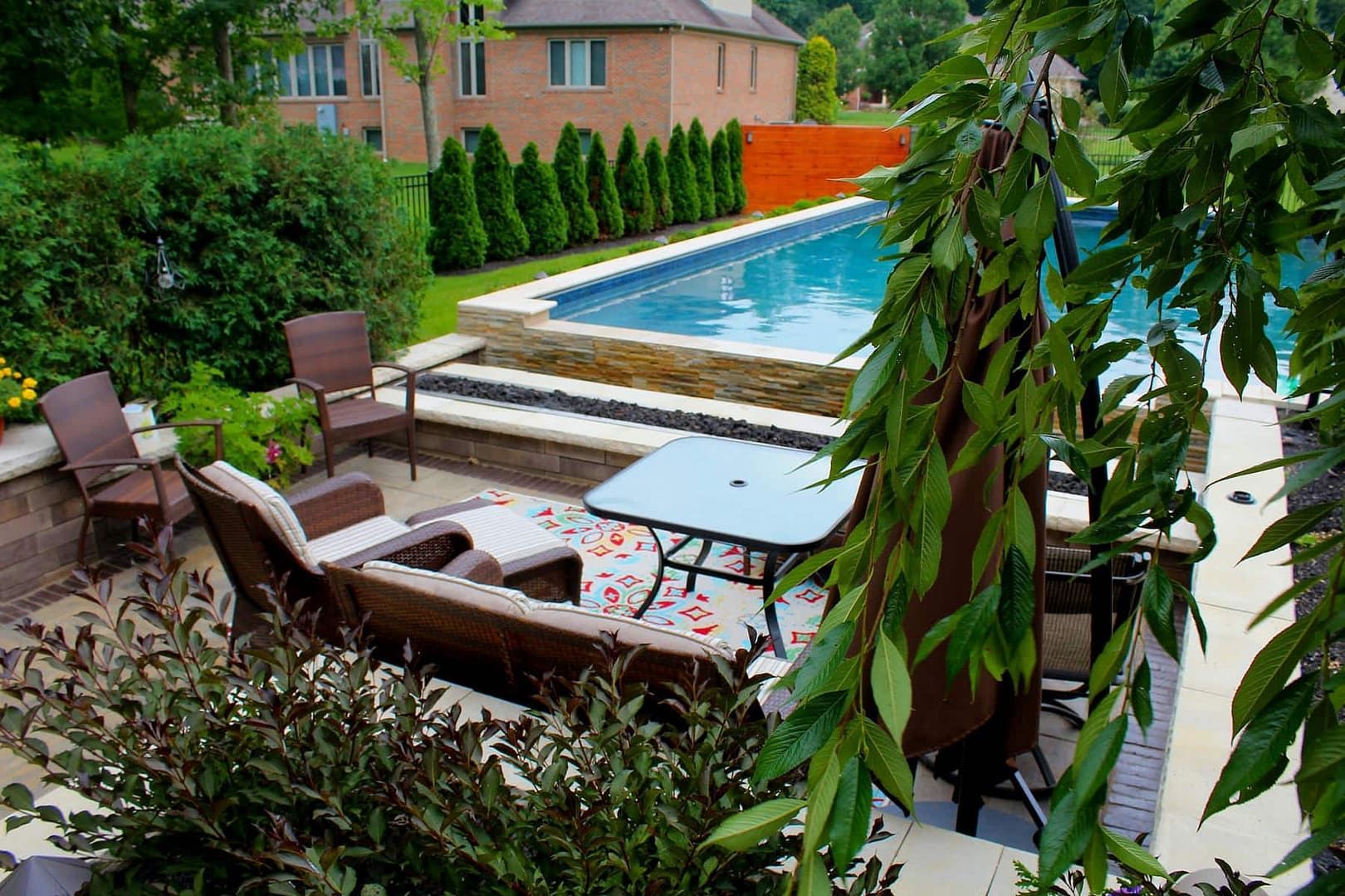 Patio with pool: seating area, lounge chairs, table, blue rectangular pool, green landscaping.