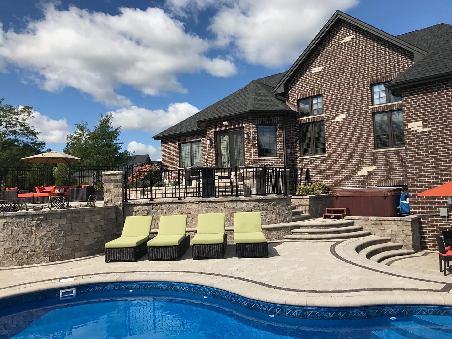 Backyard pool area with brick house; lounge chairs, patio, and hot tub.