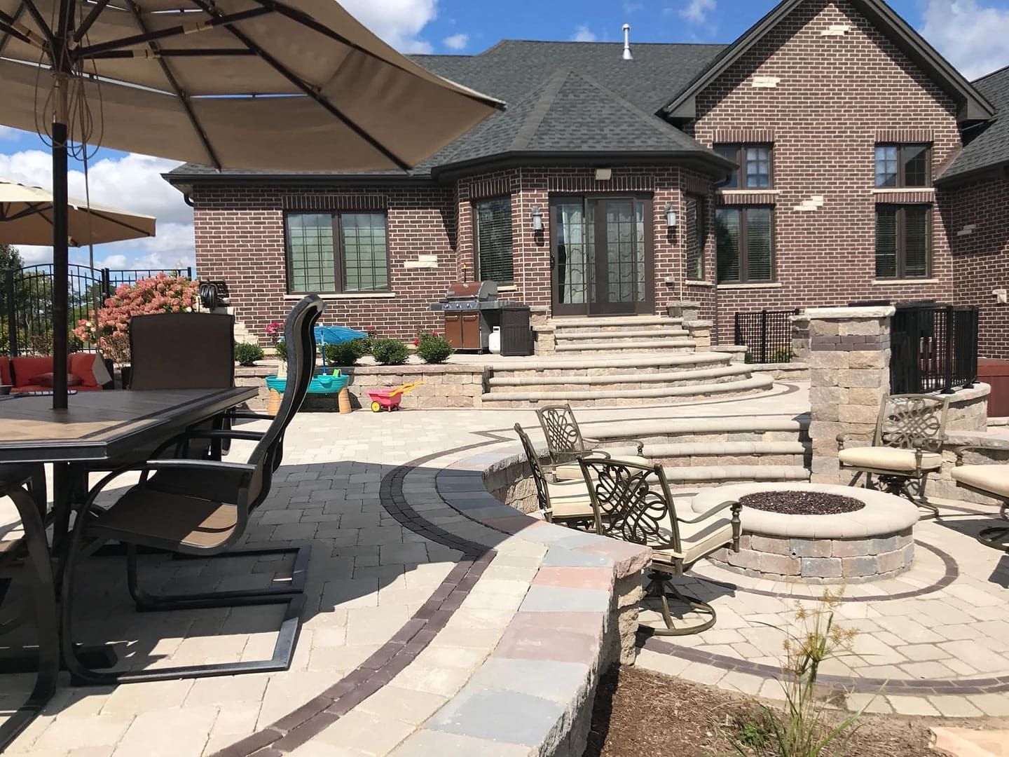 Backyard patio with brick house, fire pit, seating, dining table, and umbrellas.