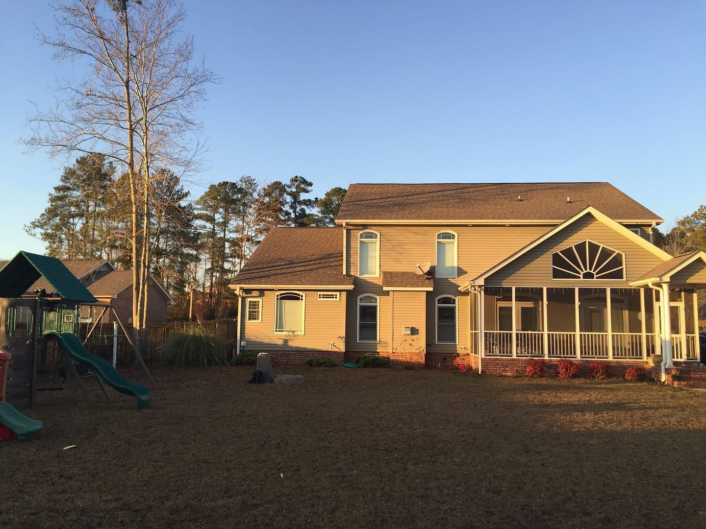 Backyard of a beige house with a screened porch and a playground on a sunny day.