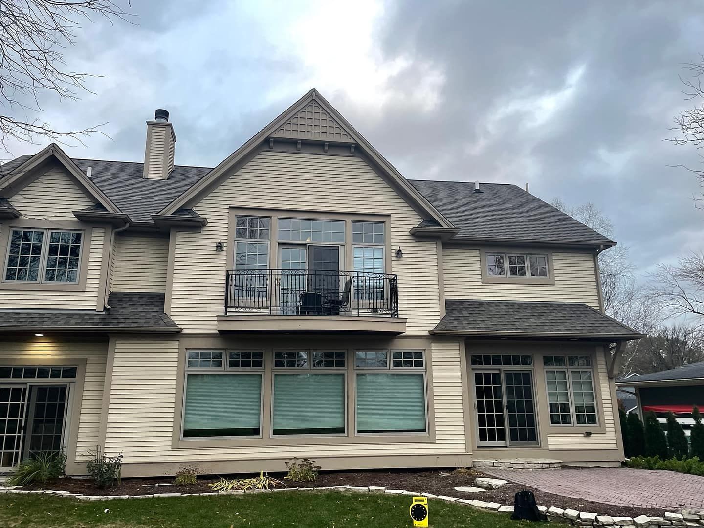 Beige house with gray roof, balcony, and windows under a cloudy sky.