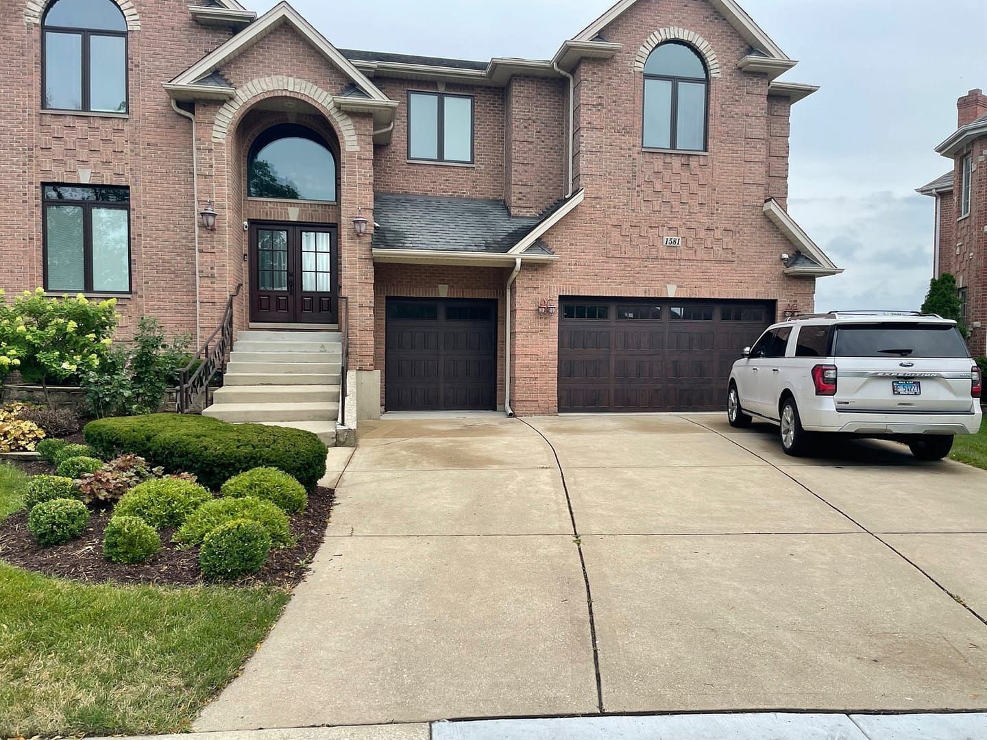 Brick house with brown garage doors; white SUV parked in driveway.