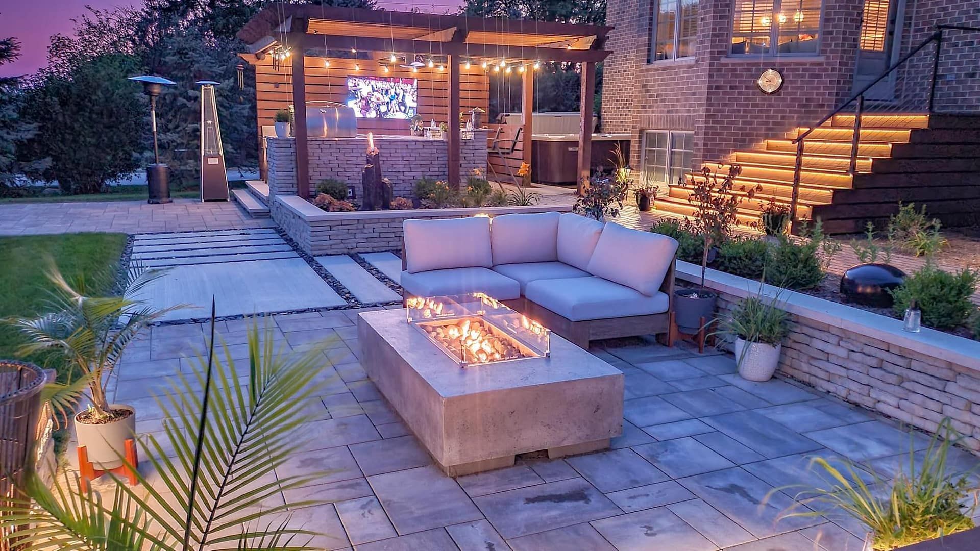 Outdoor patio with a lit fire pit, seating, and a bar area with a TV under a pergola.