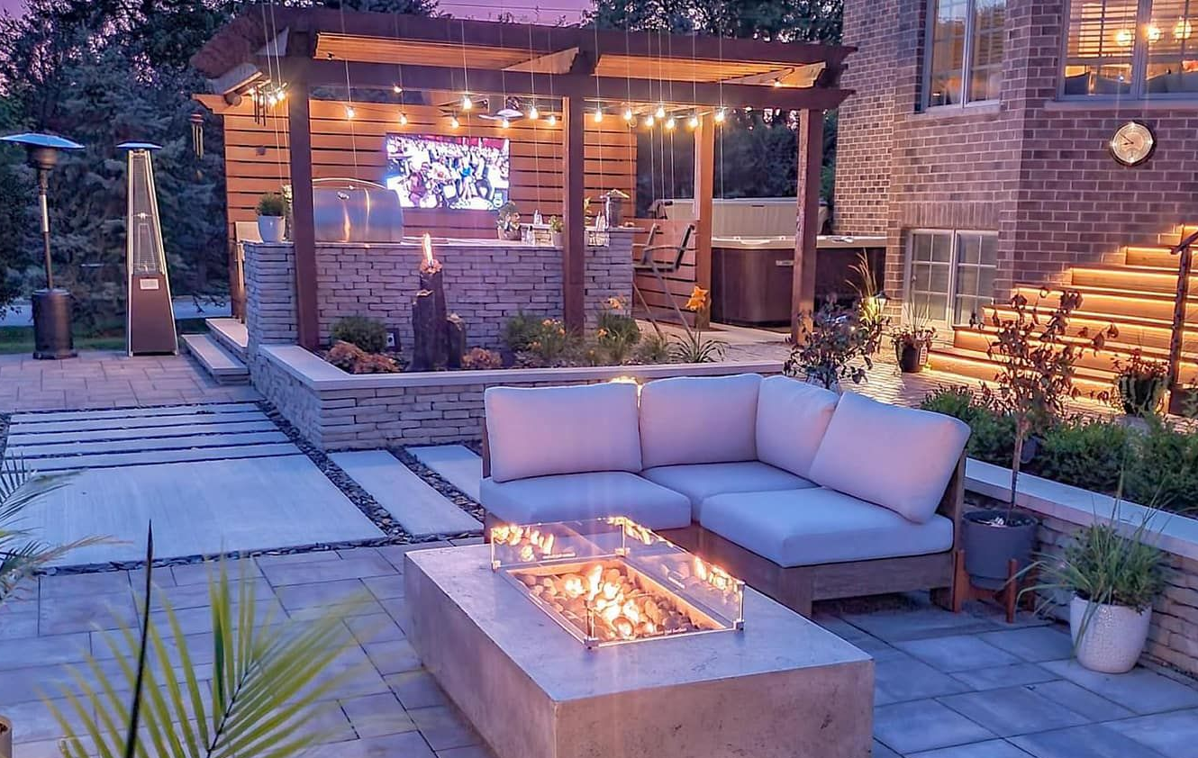 Outdoor patio with a fire pit, seating area, bar, and pergola with string lights at dusk.