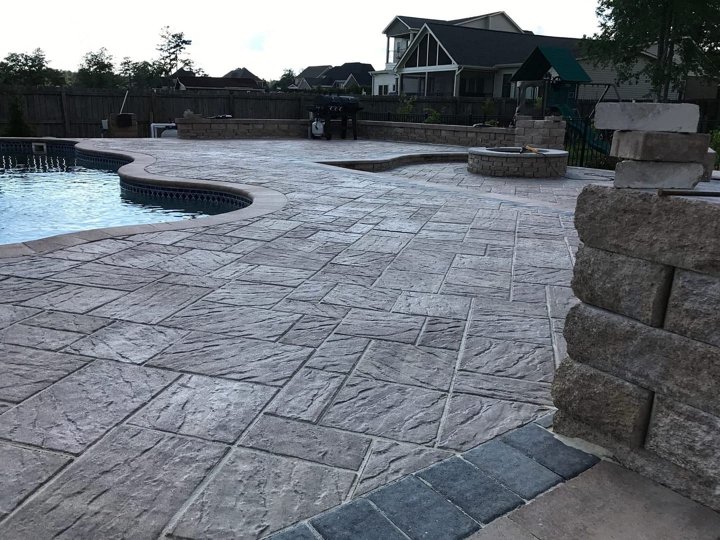 Backyard patio with pool, stone pavers, fire pit, and retaining walls.