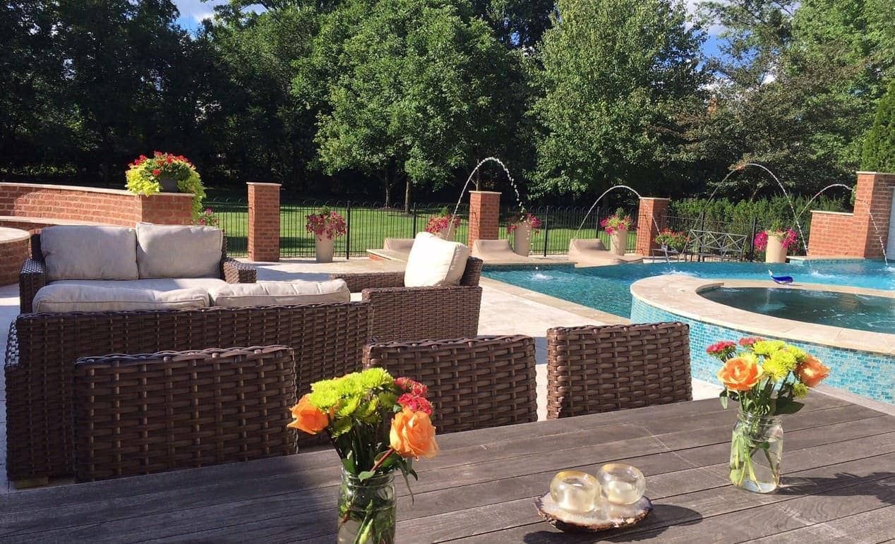 Outdoor patio with wicker furniture, a pool with fountains, and flowers.