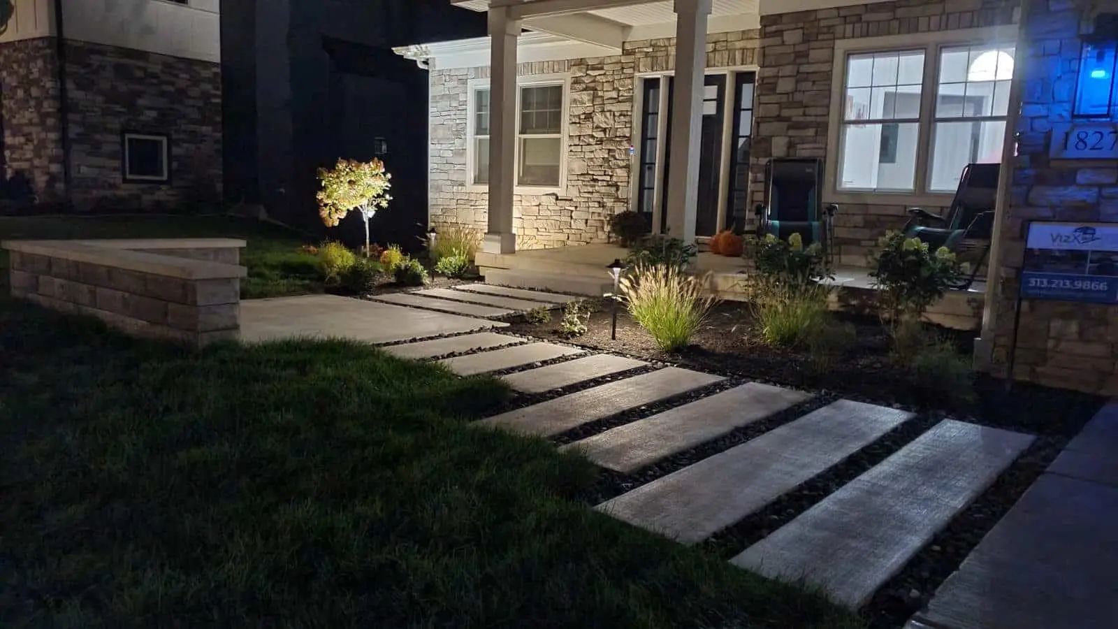 Night view of a stone walkway leading to a house with exterior lights illuminating the path and landscaping.