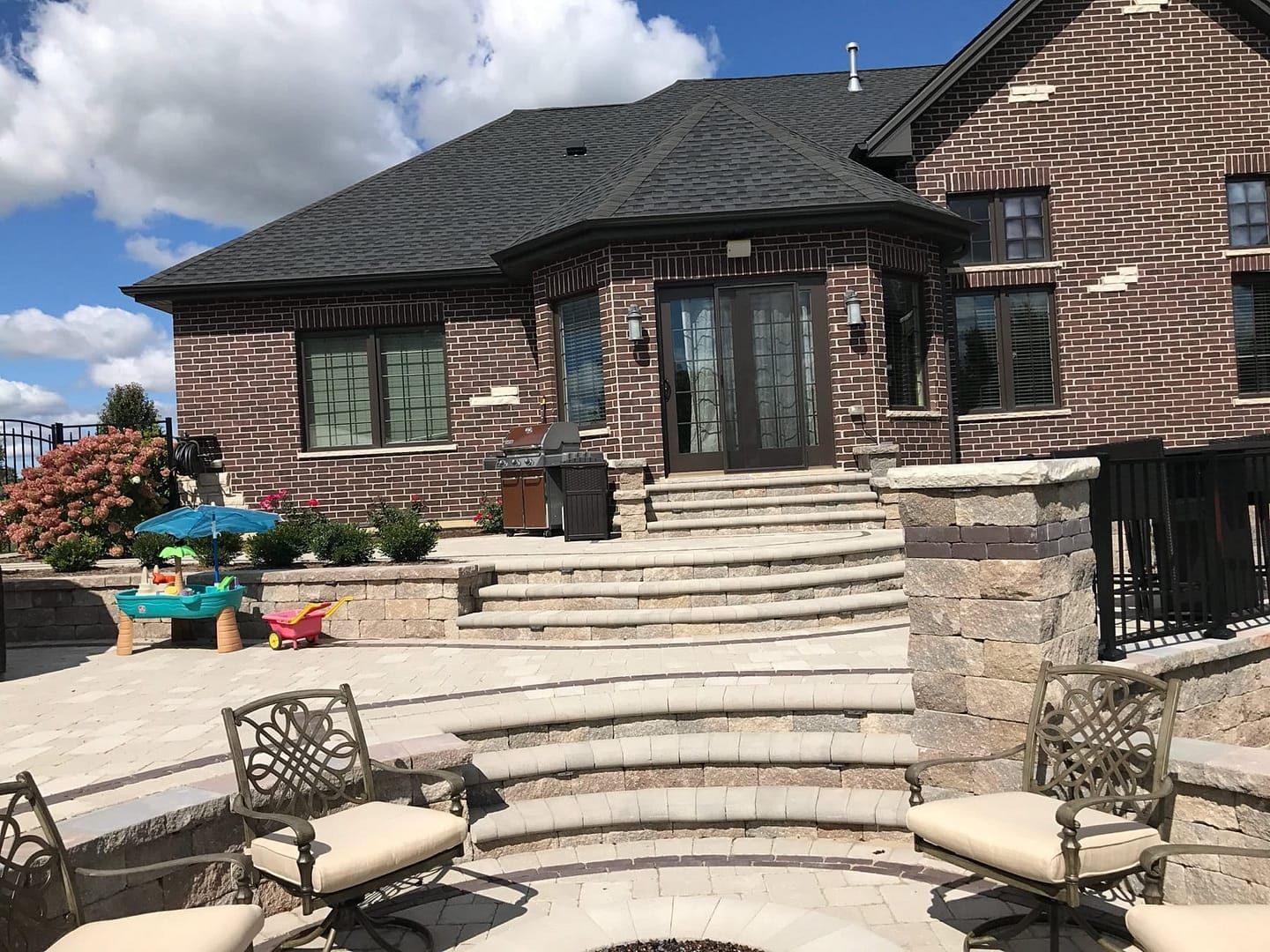 Brick house with outdoor patio, stone steps, and seating around a fire pit.