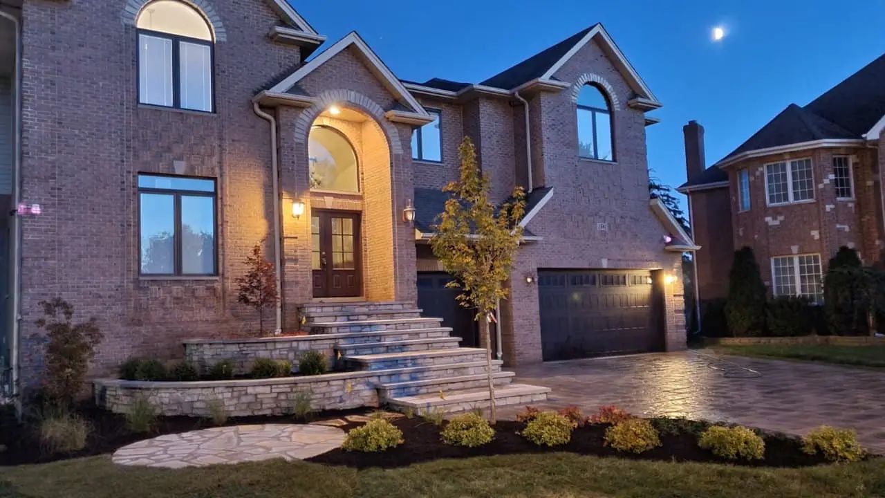 Brick house with arched entryway and multi-level stone landscaping at dusk.