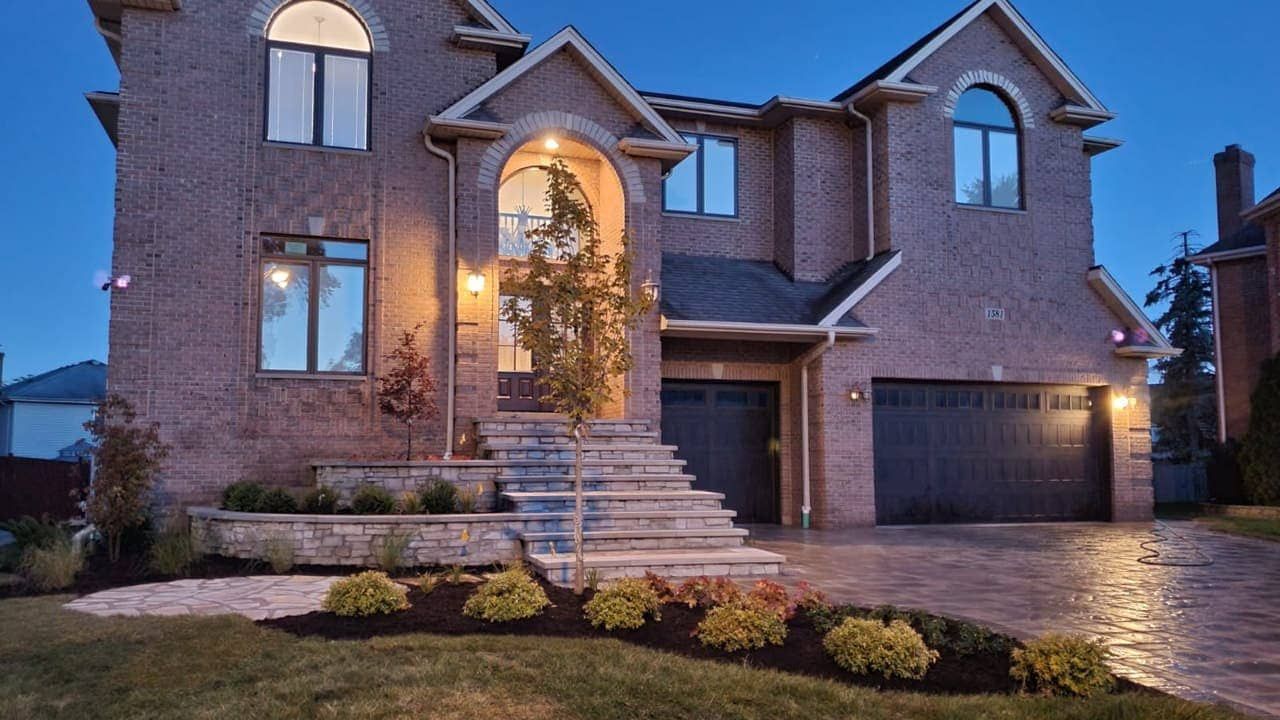 Two-story brick home at dusk with a dark garage door, steps, and landscaping.