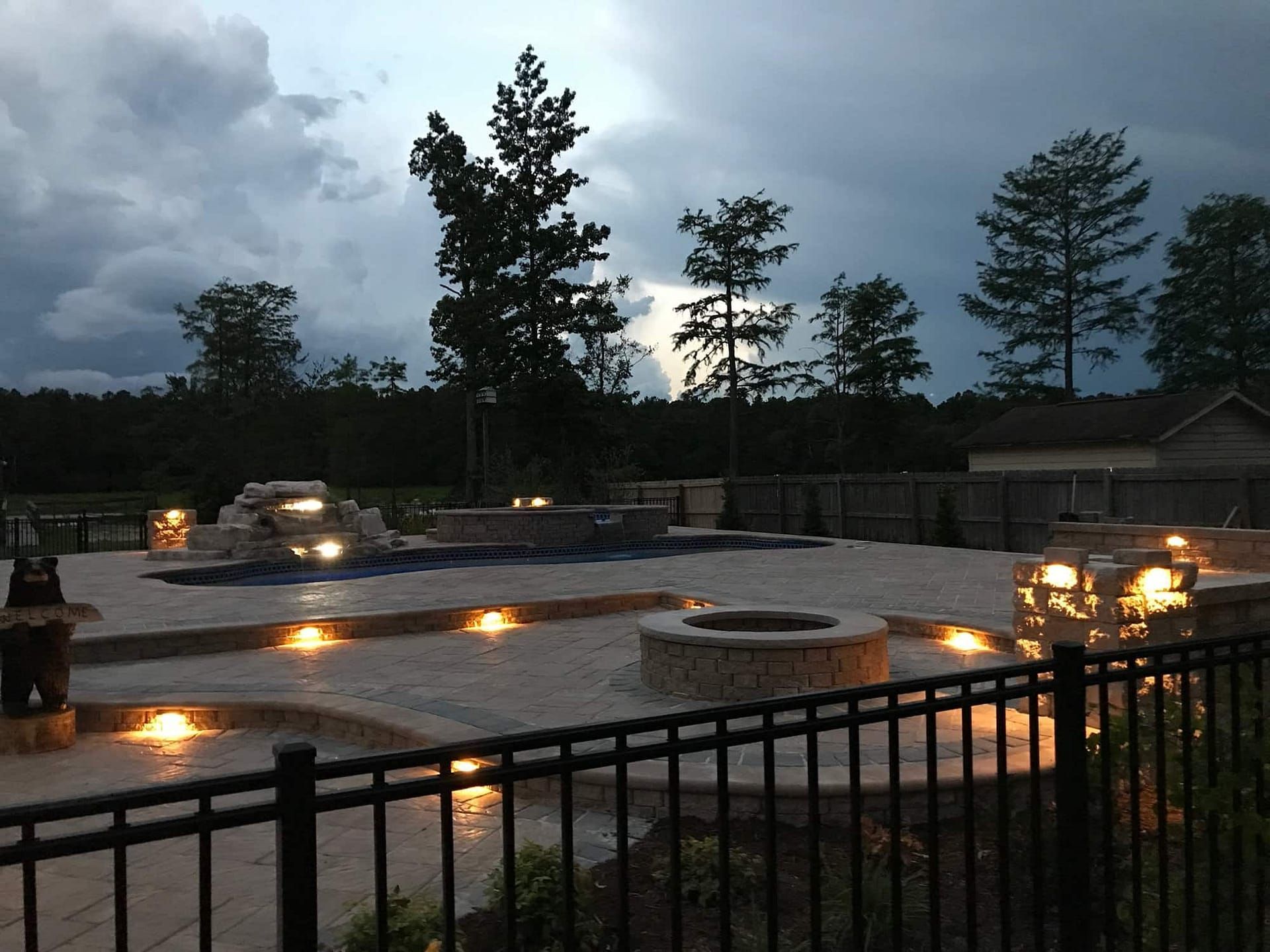 A lit outdoor patio with a fire pit and pool under a stormy sky.