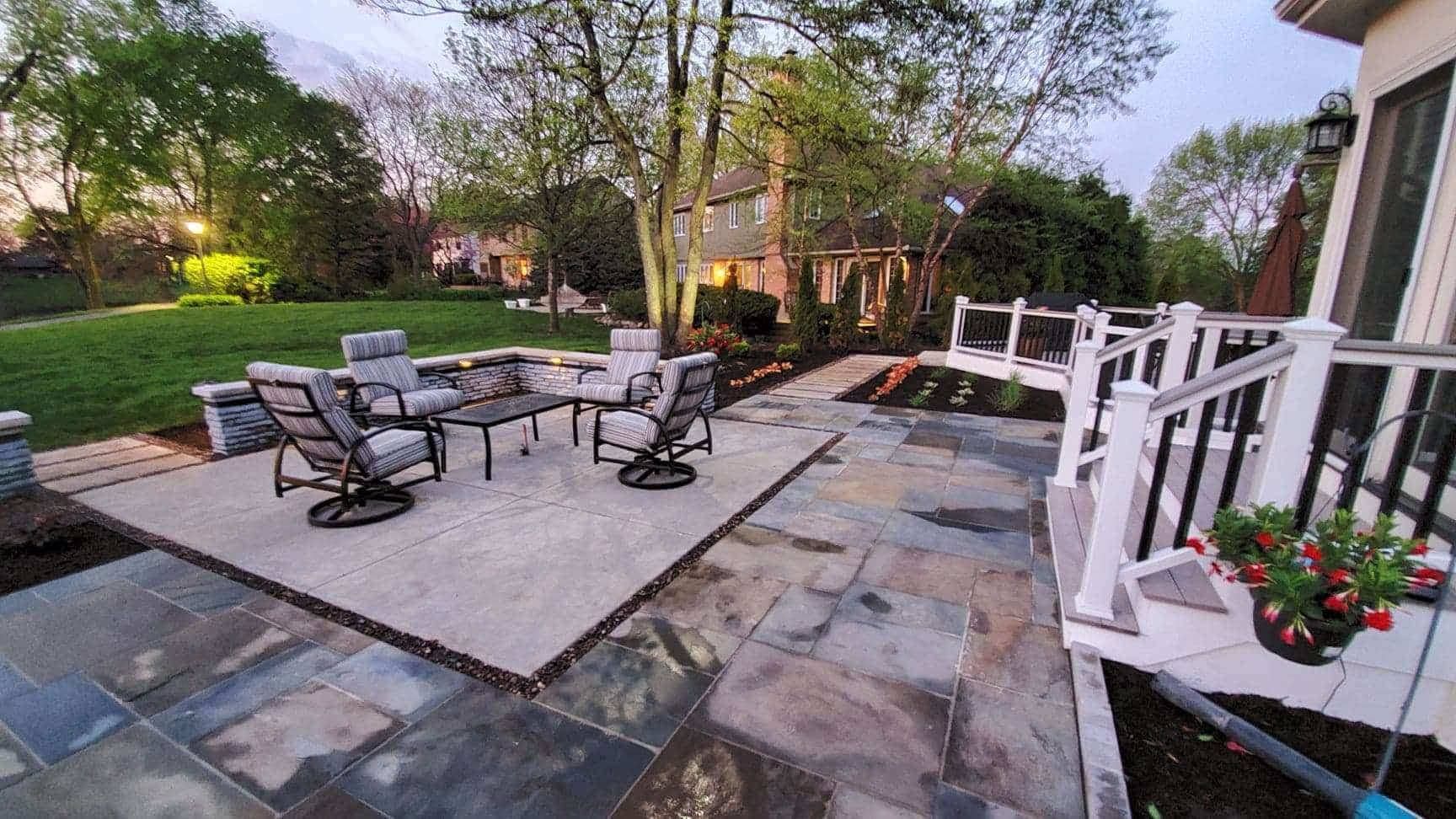 Patio with seating area, dark stone pavers, and a white deck railing, yard with grass and trees.