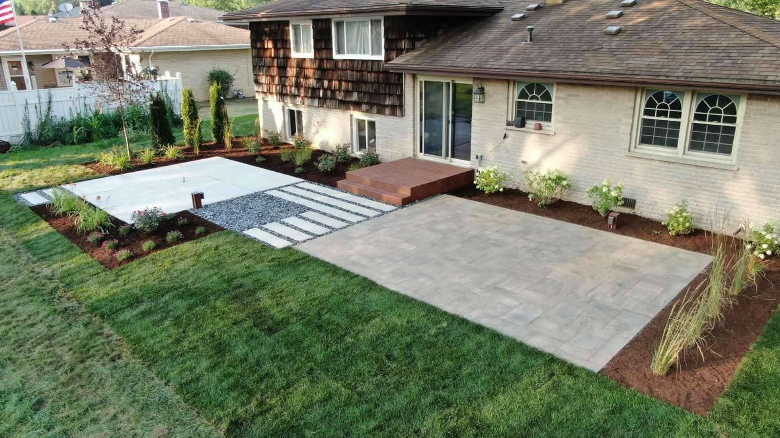 Backyard patio with concrete and stone, surrounded by grass and landscaping.