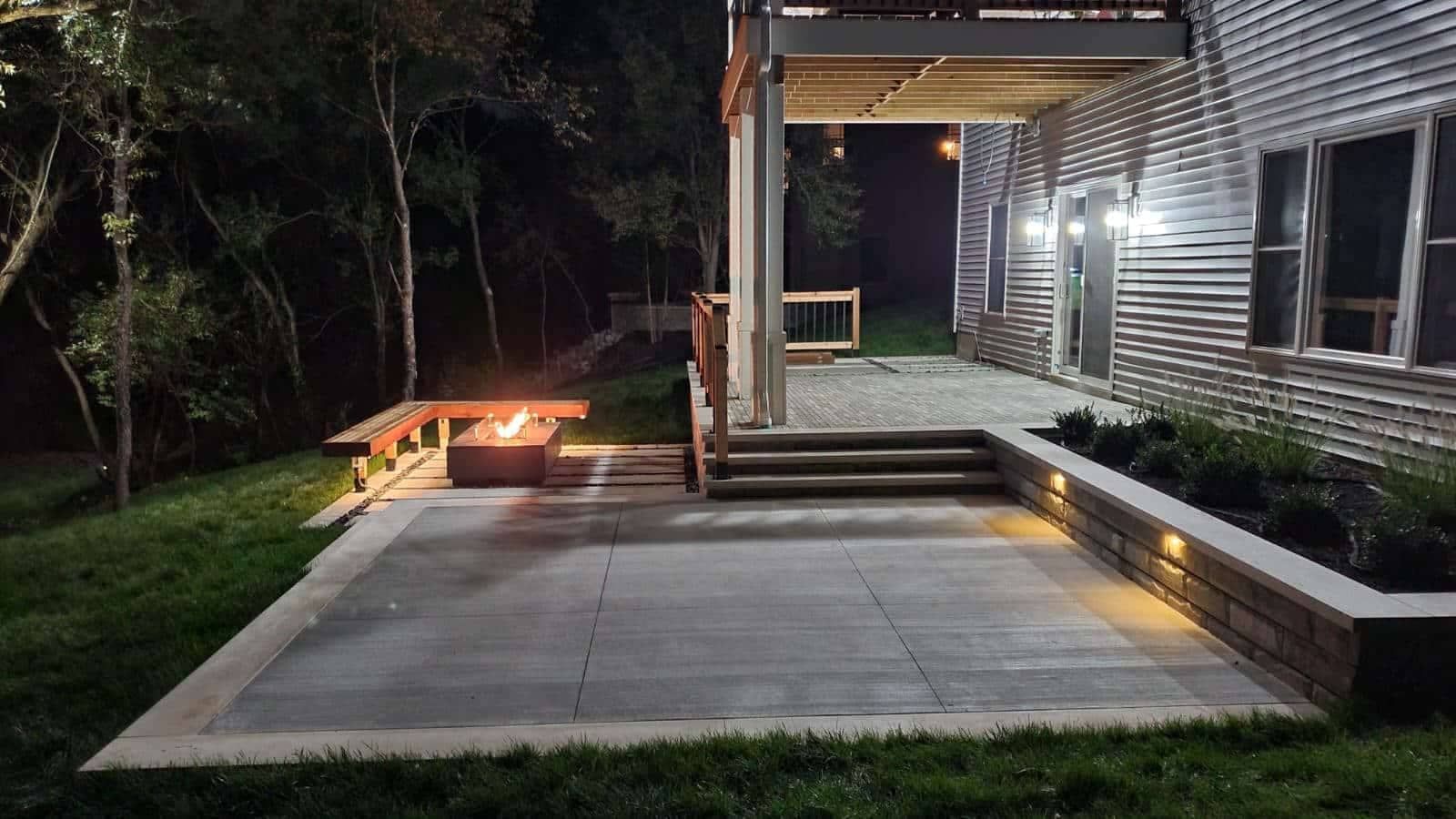 Nighttime outdoor scene: patio with fire pit, steps to covered area, and house with lights.