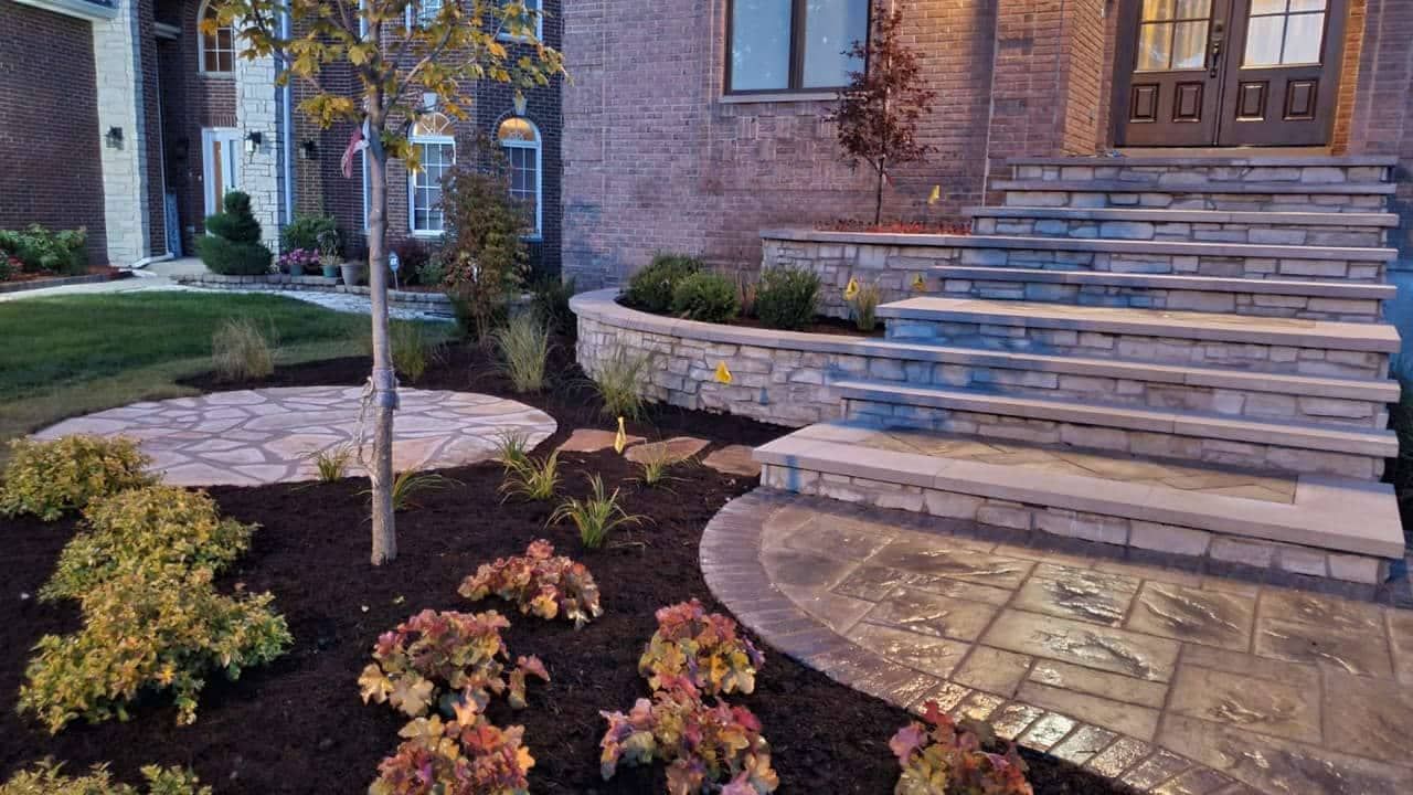 Stone steps lead to a house with a landscaped front yard, including plants and a circular patio.