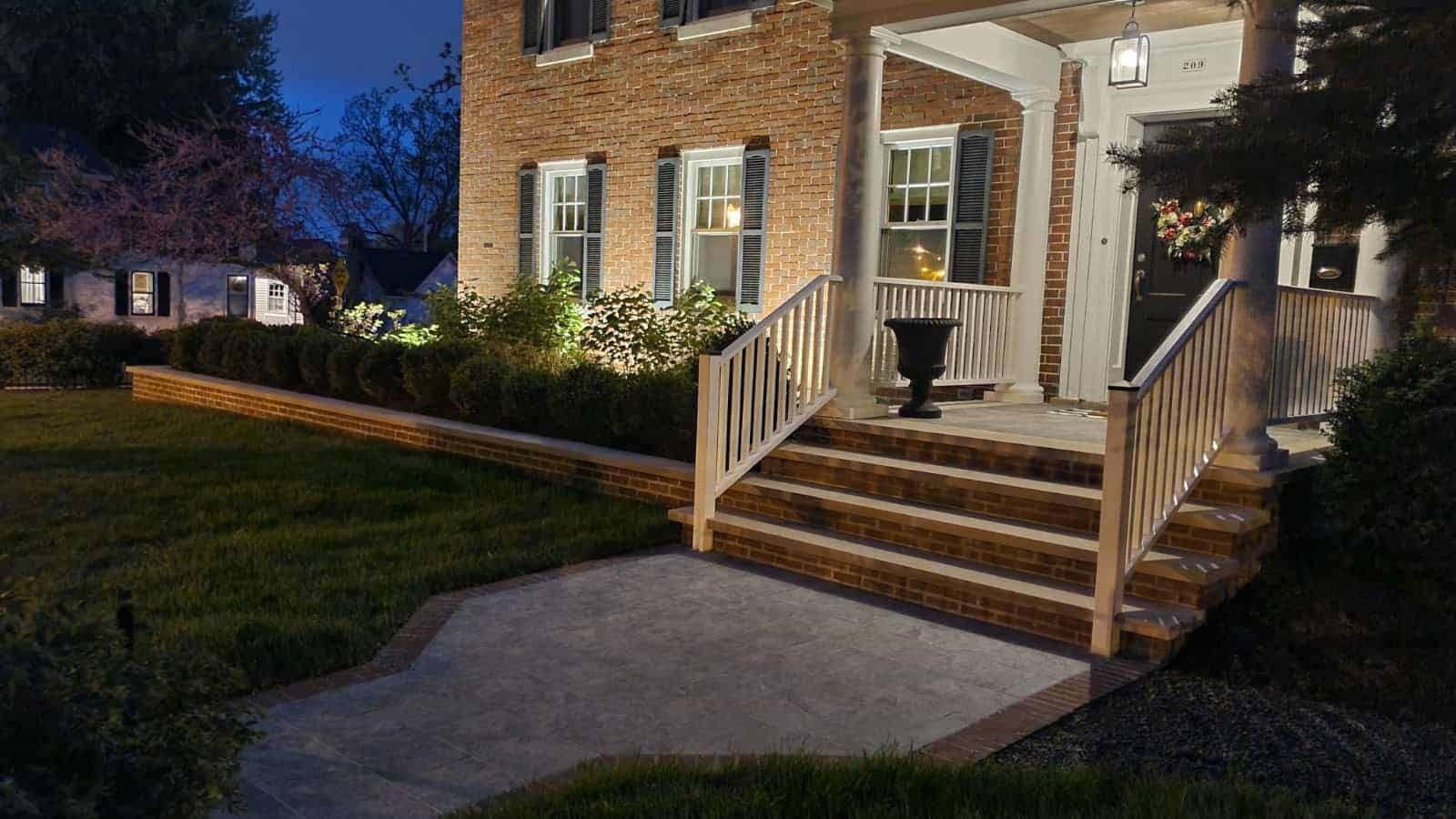 Brick house lit up at dusk with a concrete walkway and steps leading to the front door.