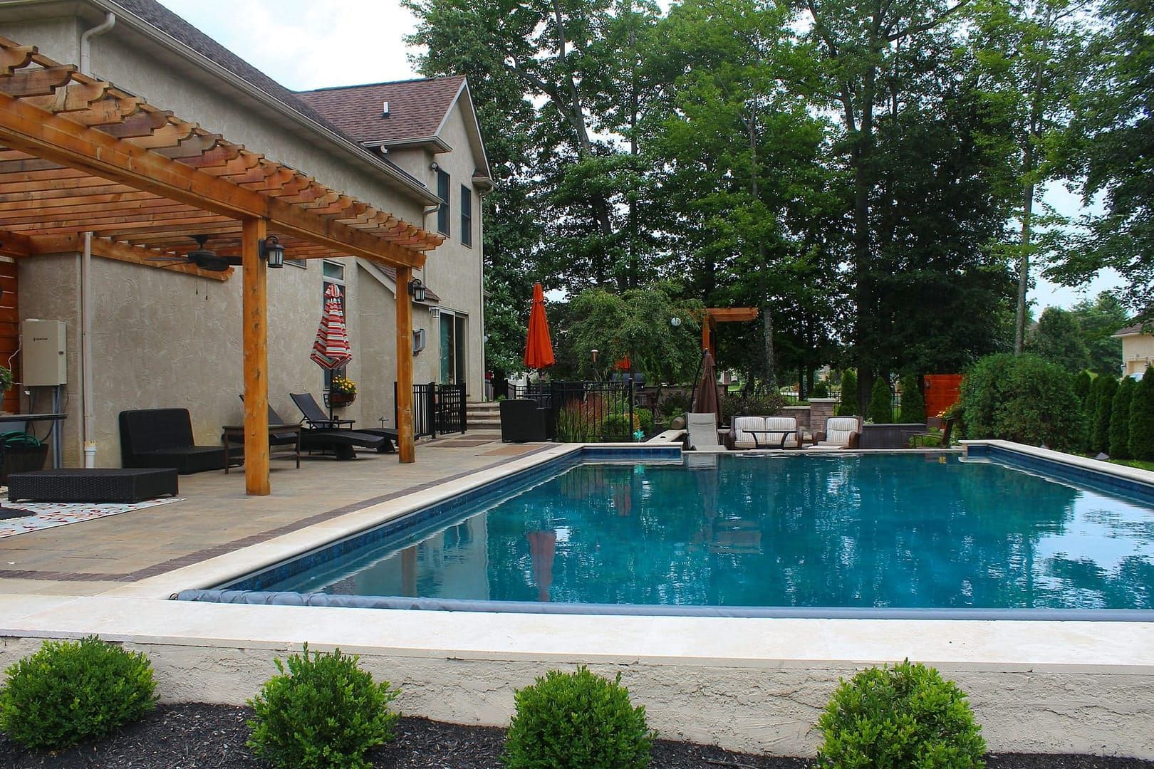 Backyard pool with a house, patio, and trees. Turquoise water.